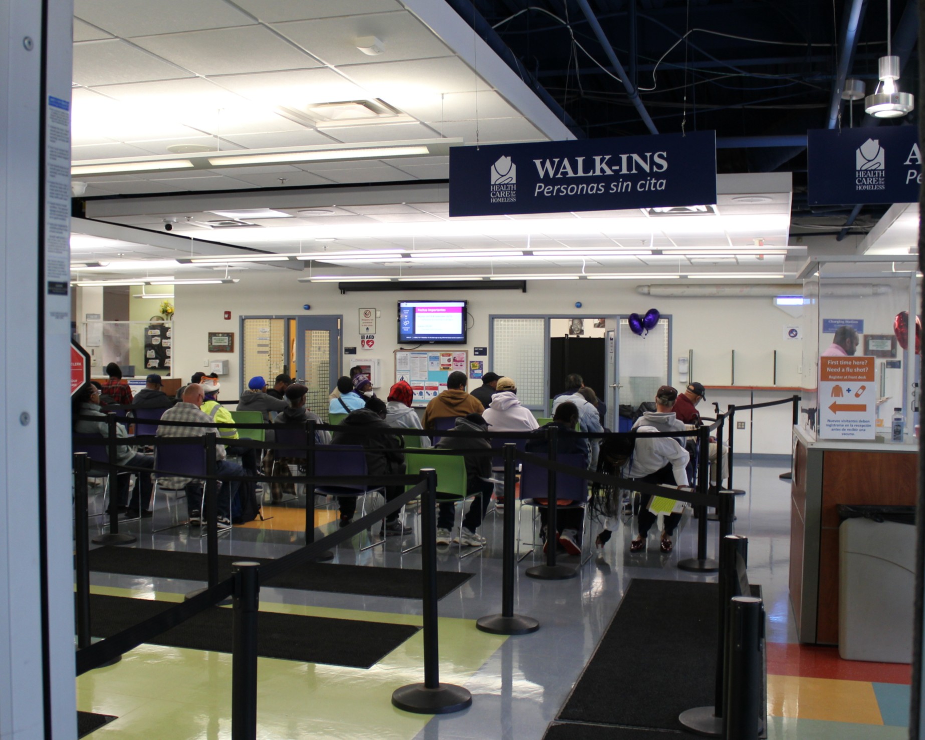 Seated people wait for their flu shots. A hanging sign reads "walk-ins."