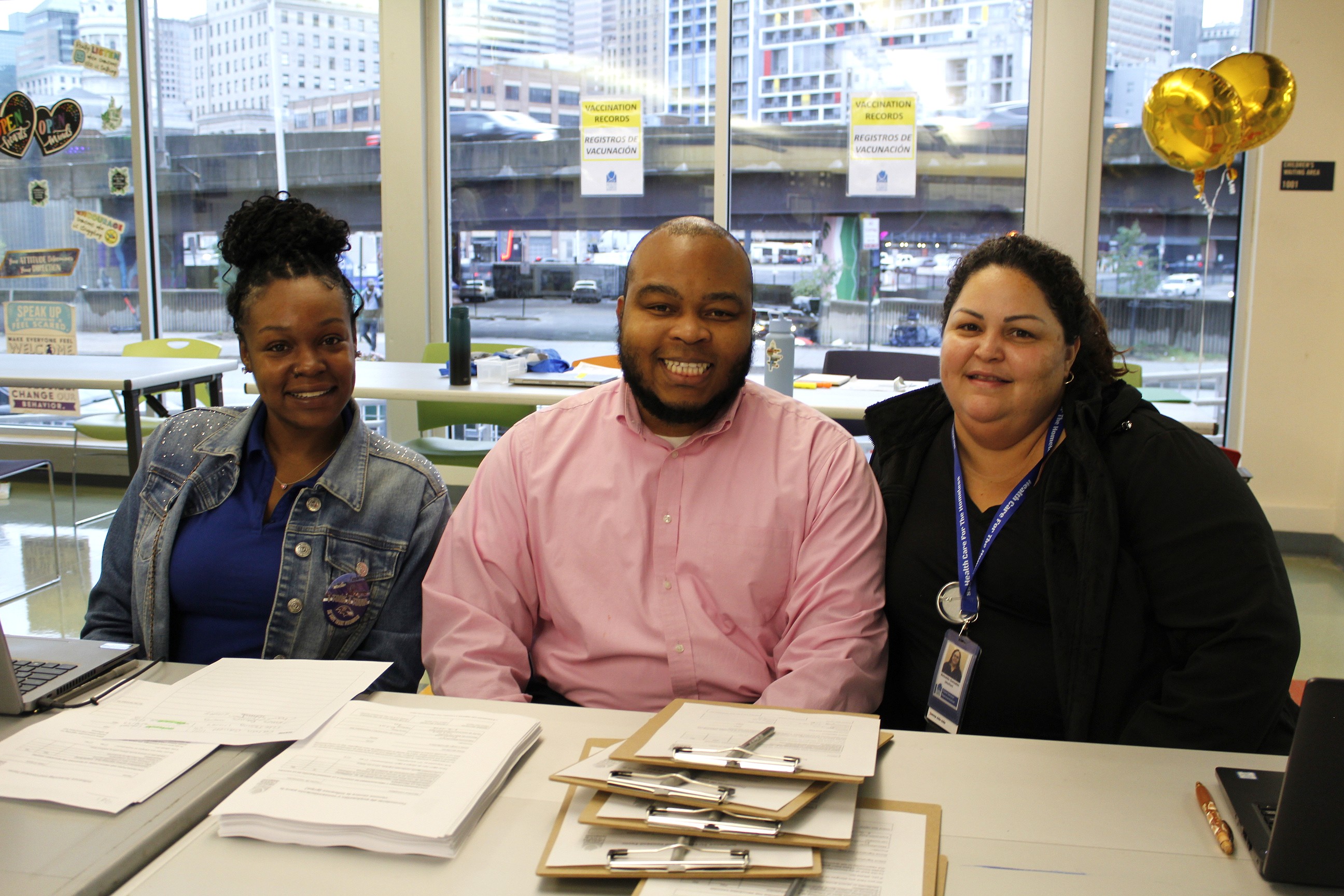 Three staff members sit at the registration table for the Coat and Flu Drive.