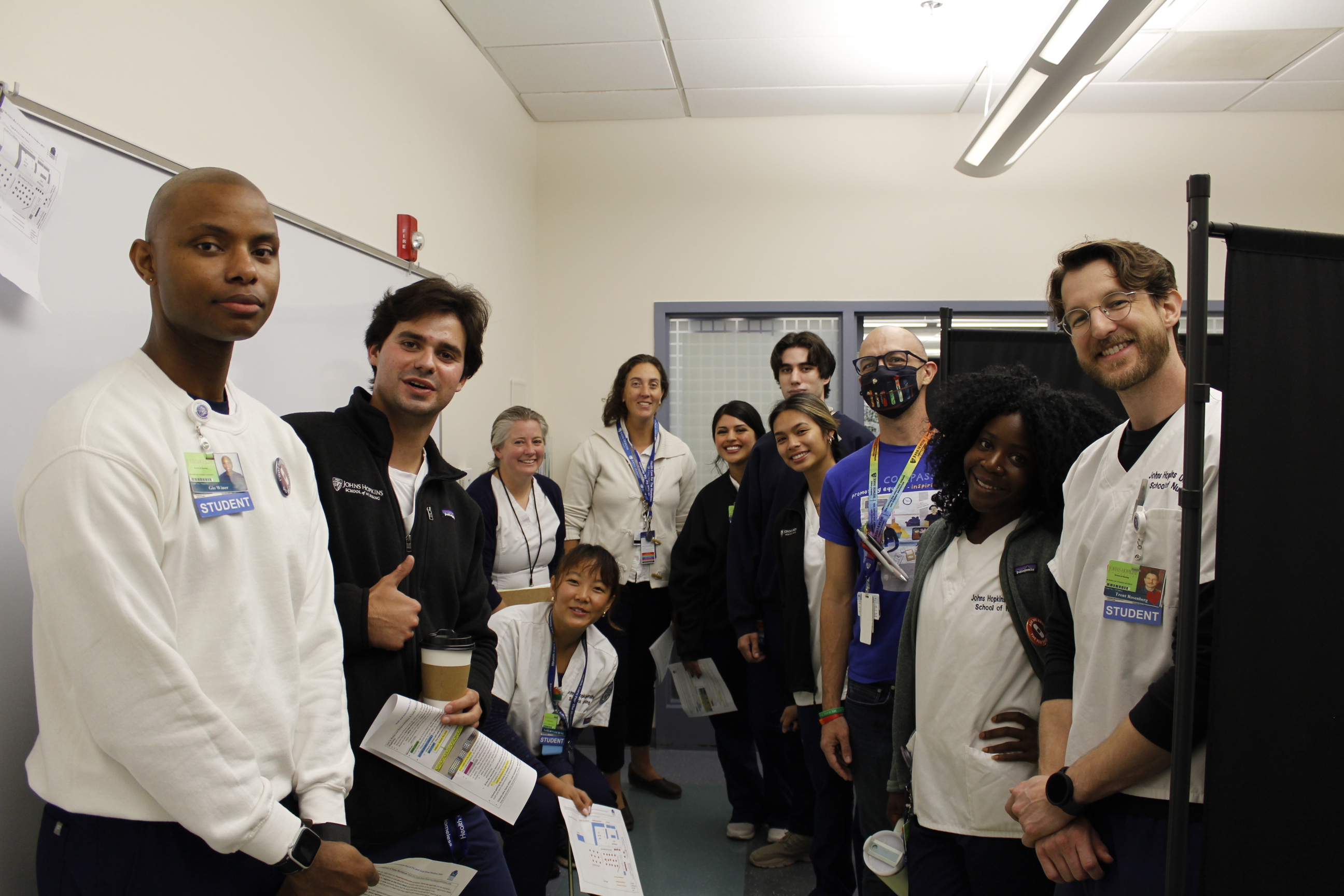 A group of volunteer nurses and students wearing scrubs gather in a small room for a photo.