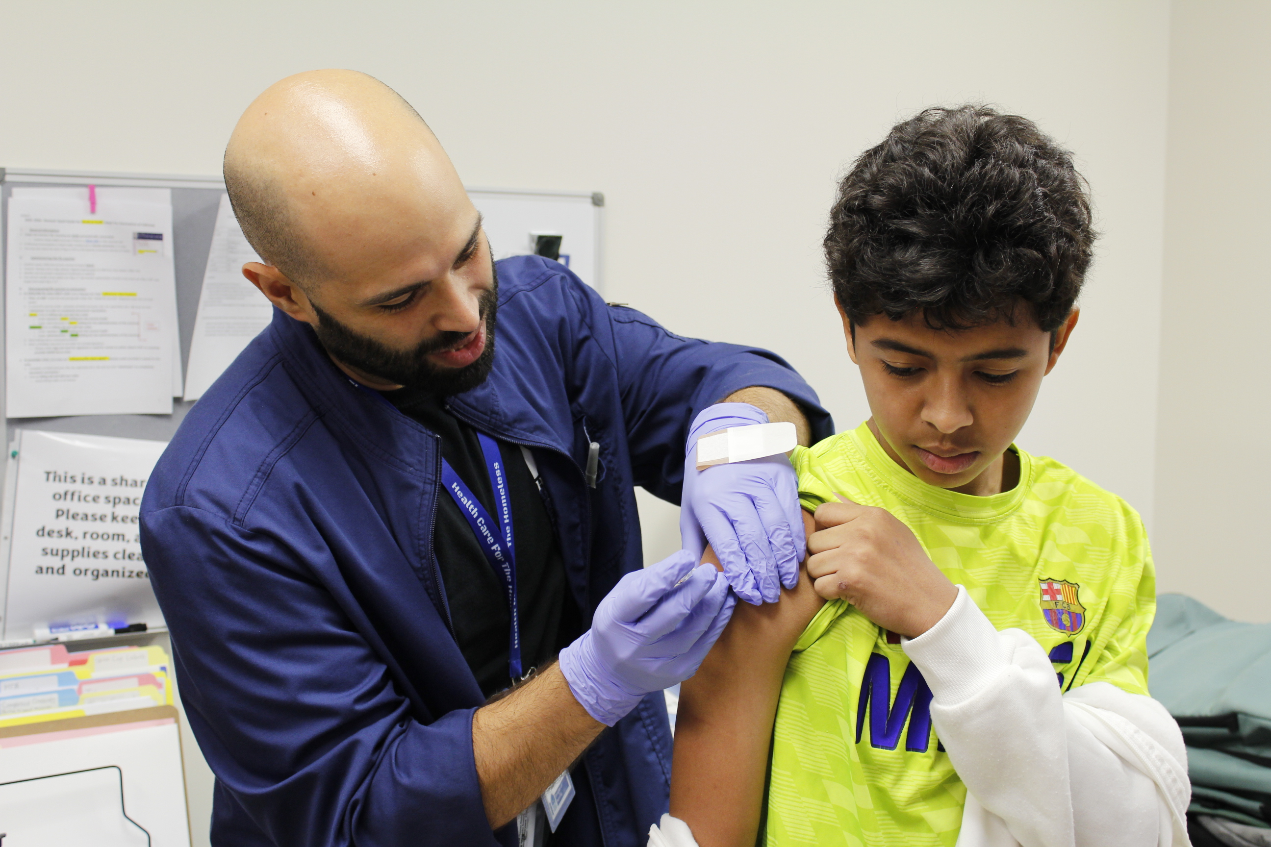 A light-skinned doctor with a dark beard administers a flu shot to a medium-skinned boy with brown hair.