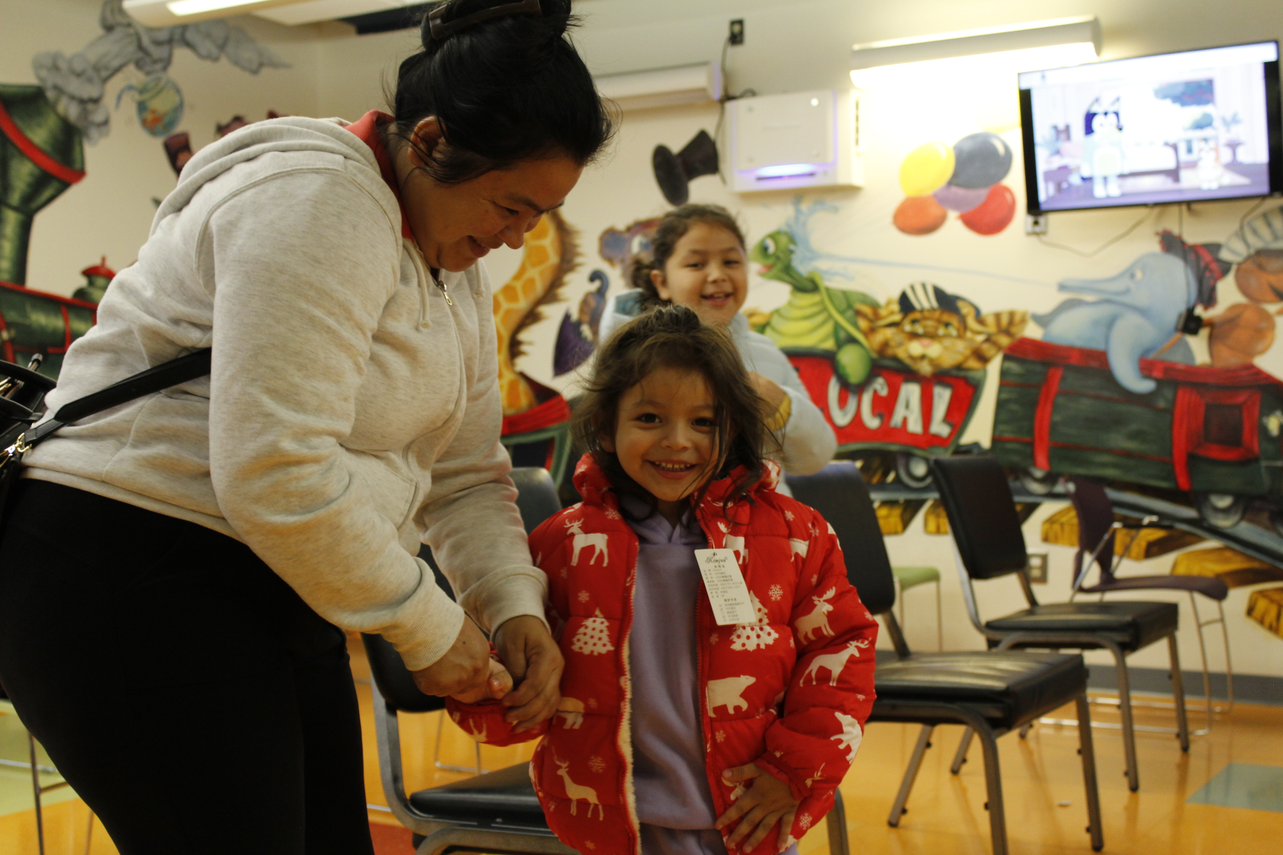 A young girl with brown hair wears a red coat and holds her mom's hand.