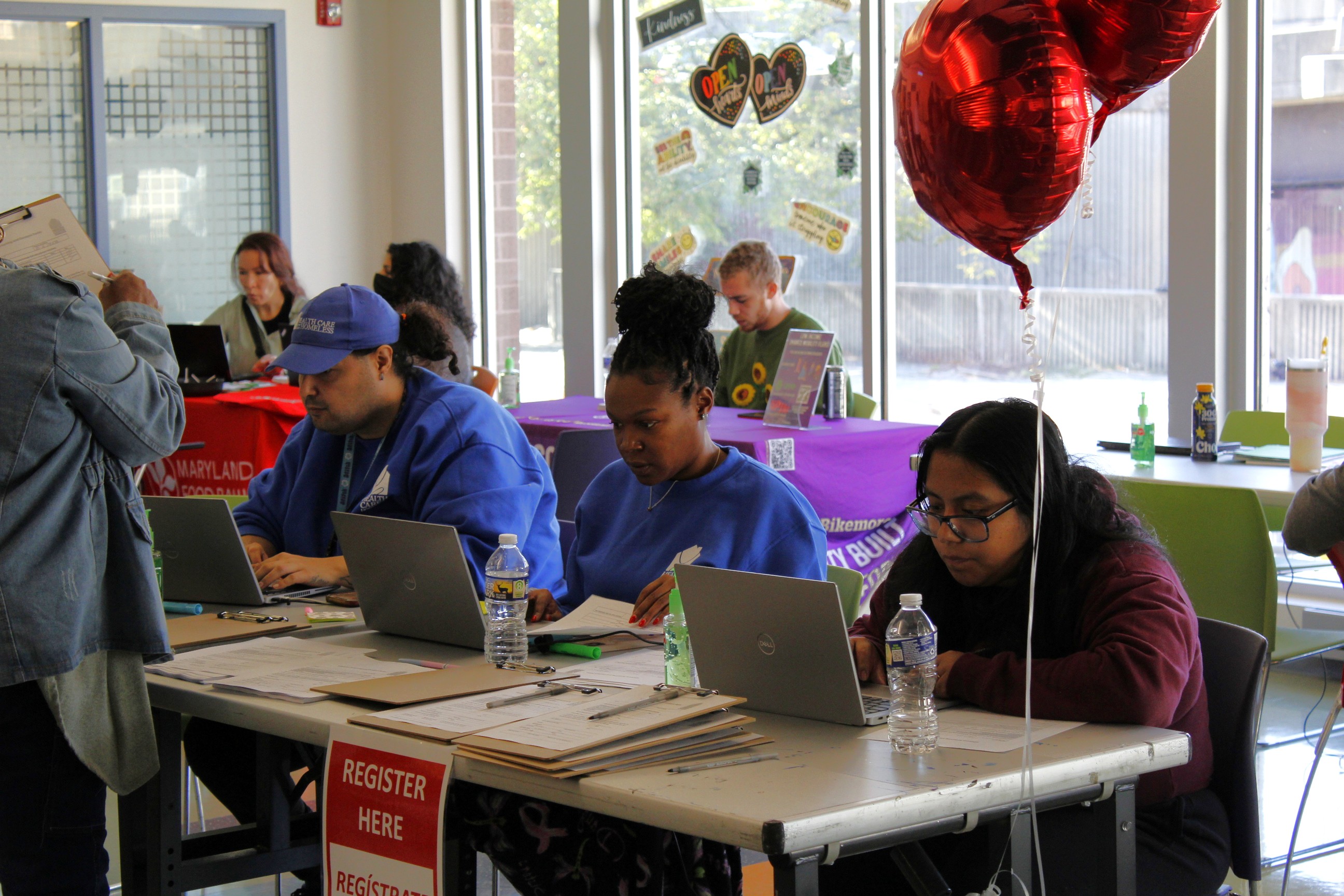 Staff members sit at the registration table with their laptops. A red balloon hovers next to the table.