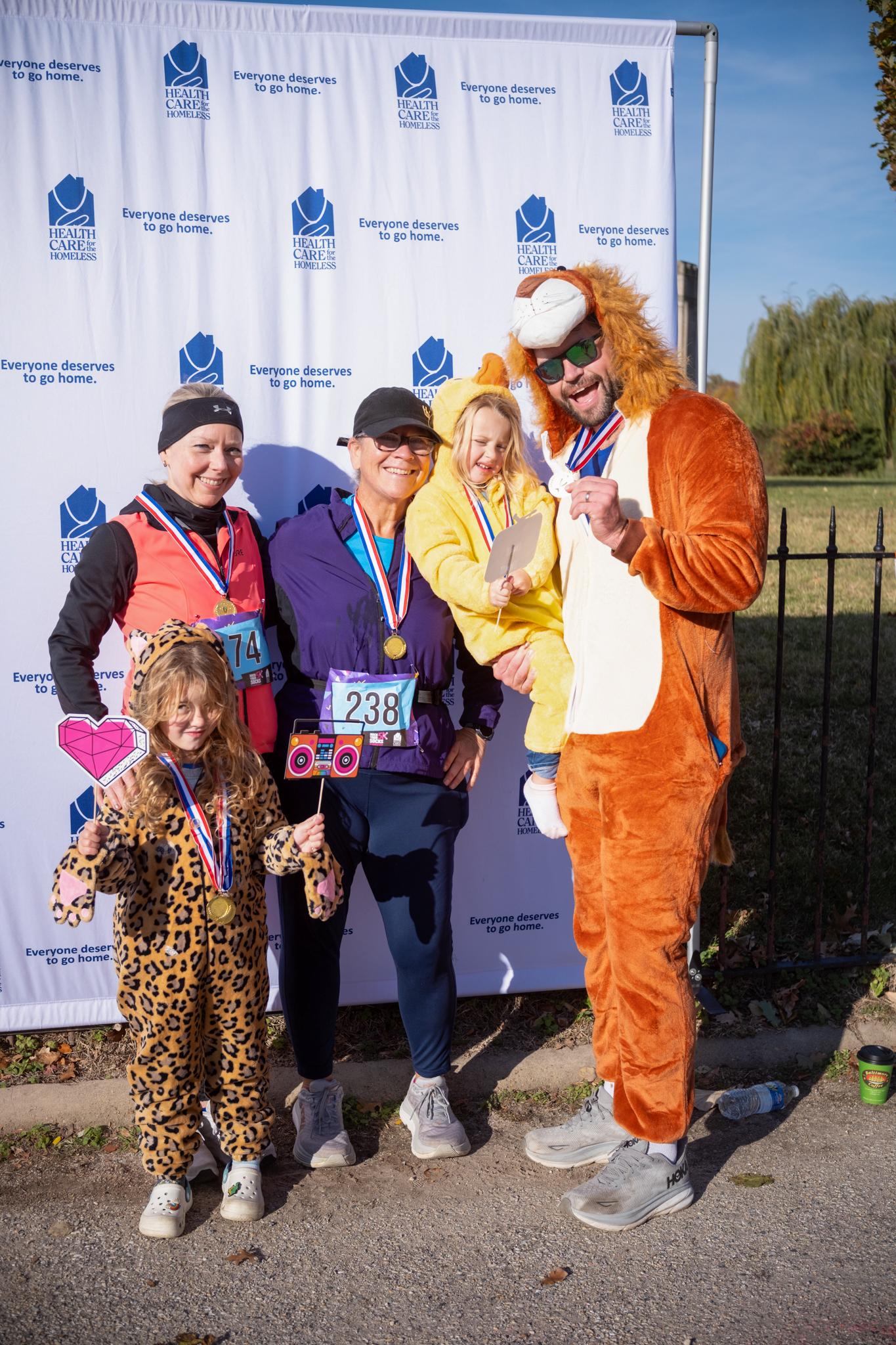 A group of adults and children in front of the Health Care for the Homeless step-and-repeat. They are wearing Halloween costumes.