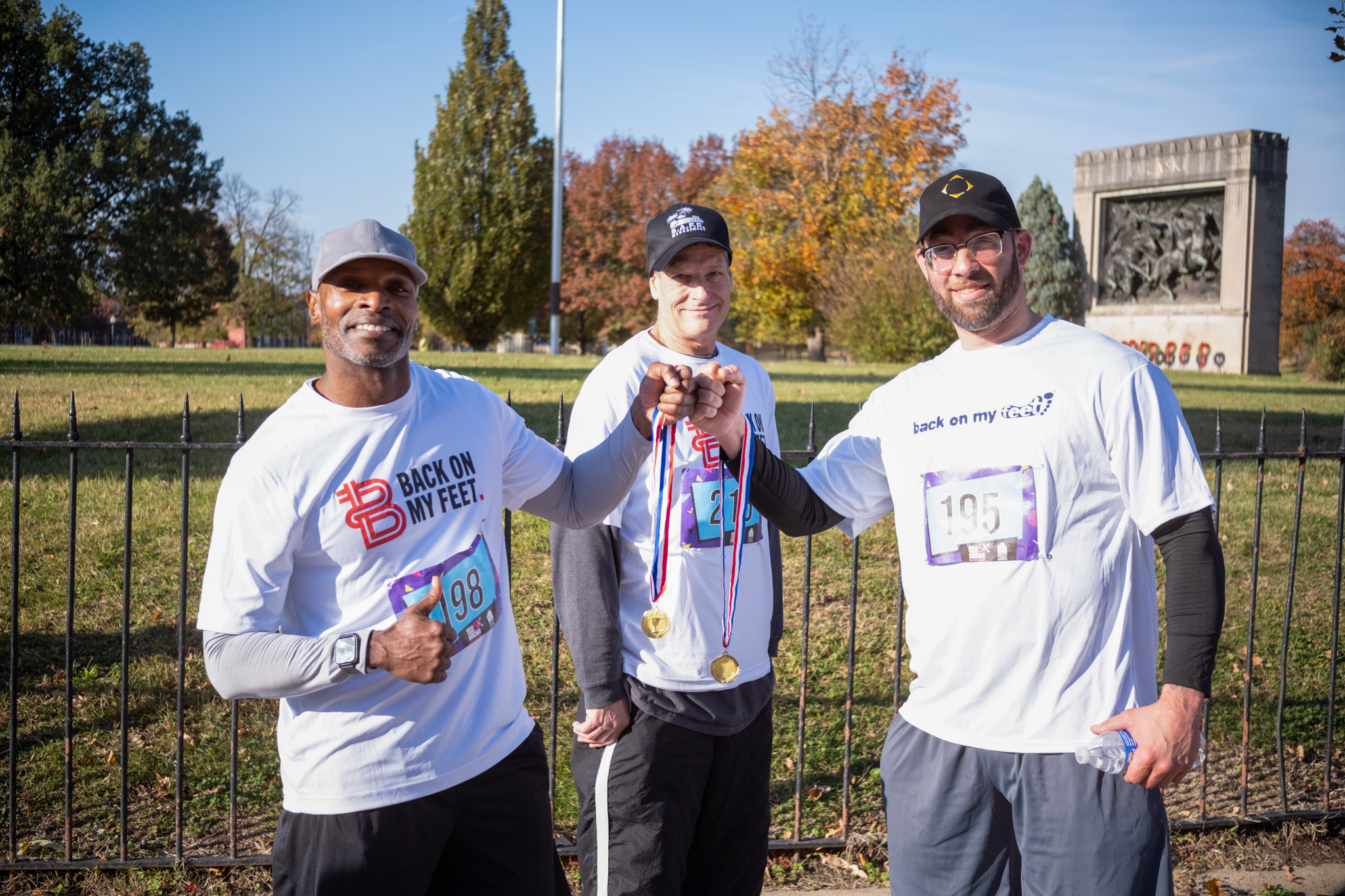 A group of three people tap their running medals together.