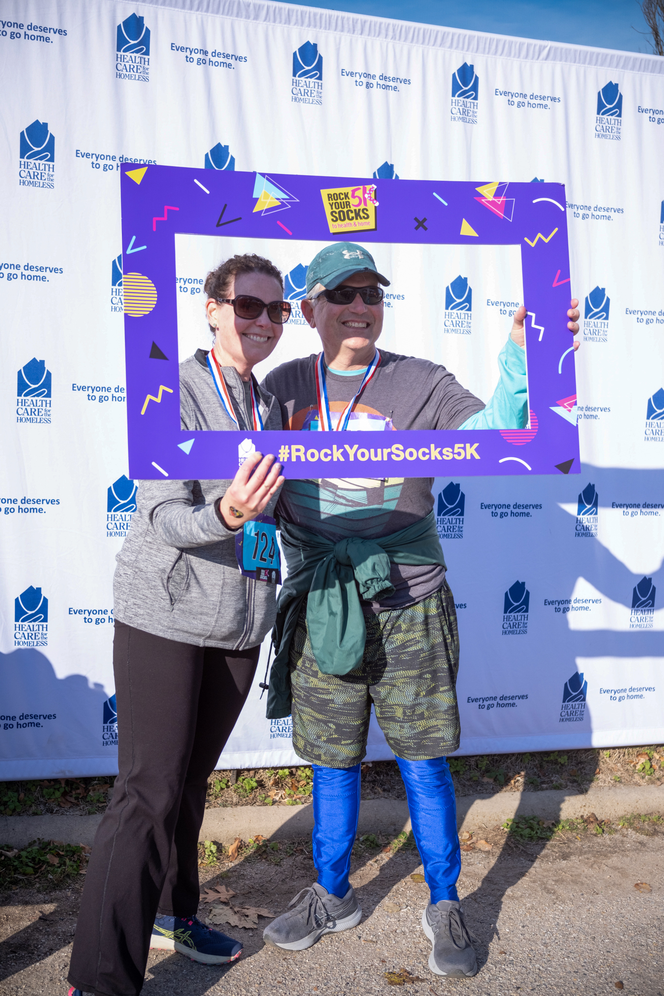 Two light-skinned people in front of the Health Care for the Homeless step-and-repeat hold a large photo frame cut-out.