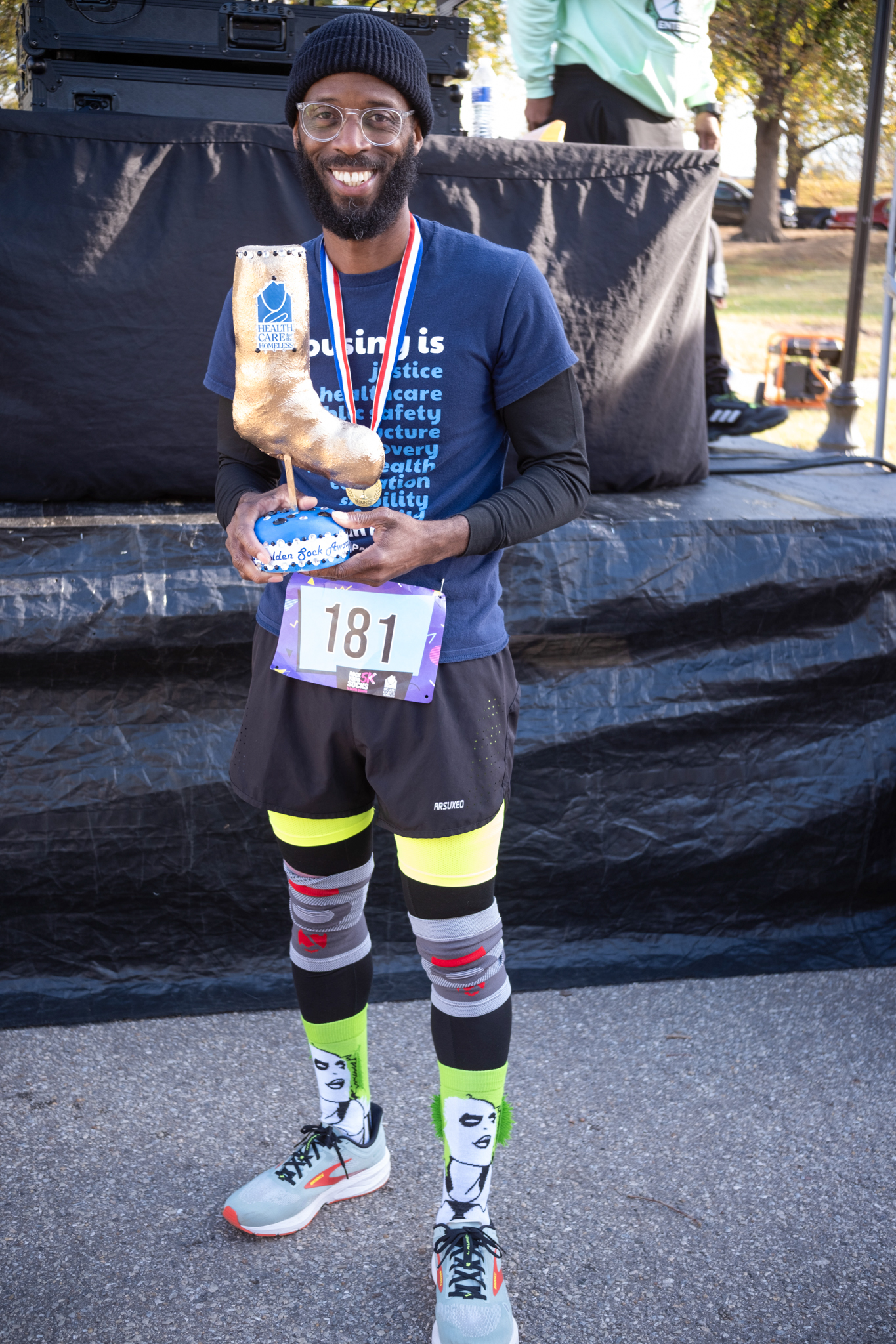 A dark-skinned man wearing a hat and colorful socks holds the Golden Sock Award.