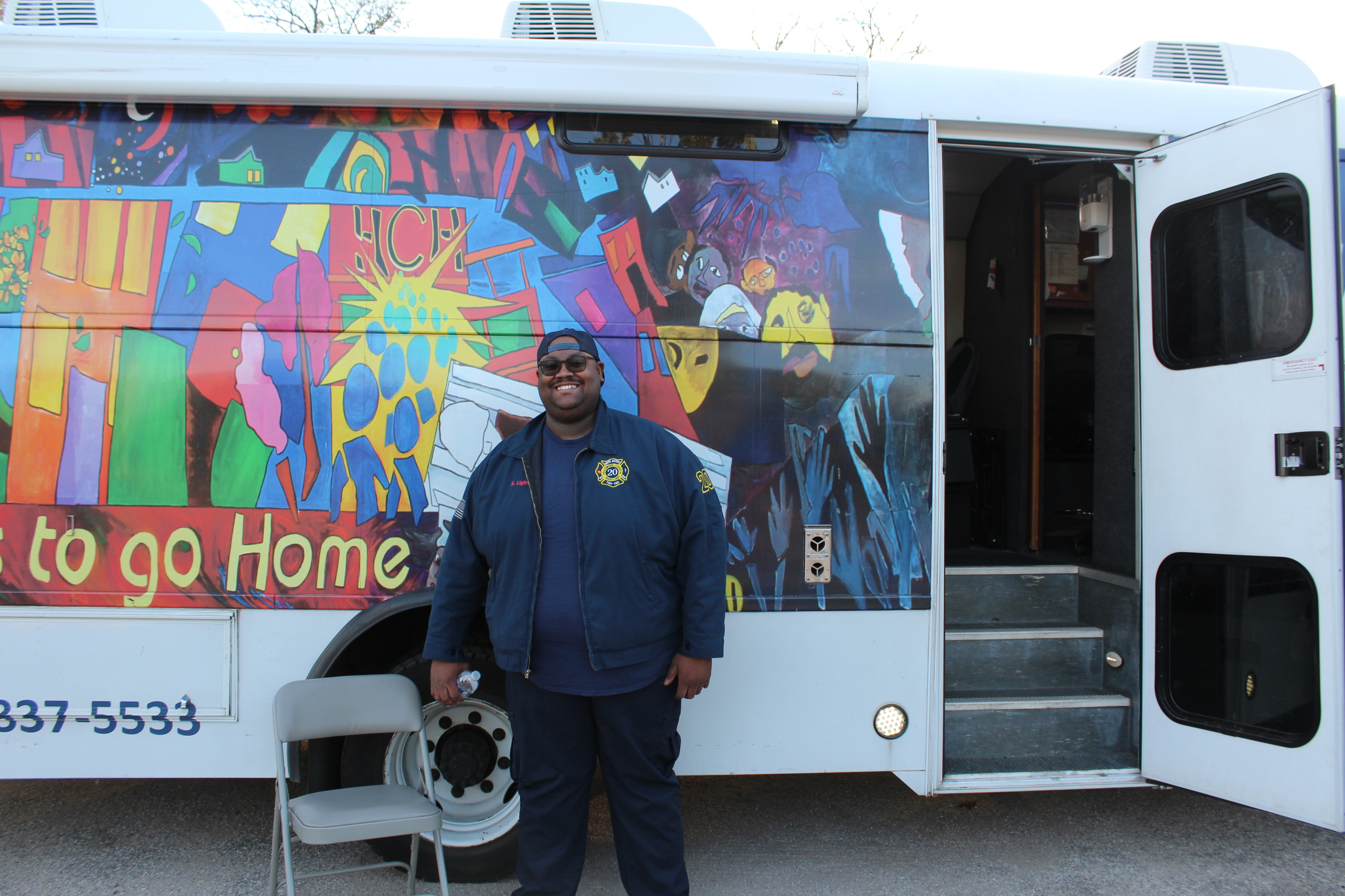 A dark-skinned man stands in front of Health Care for the Homeless's Mobile Clinic.