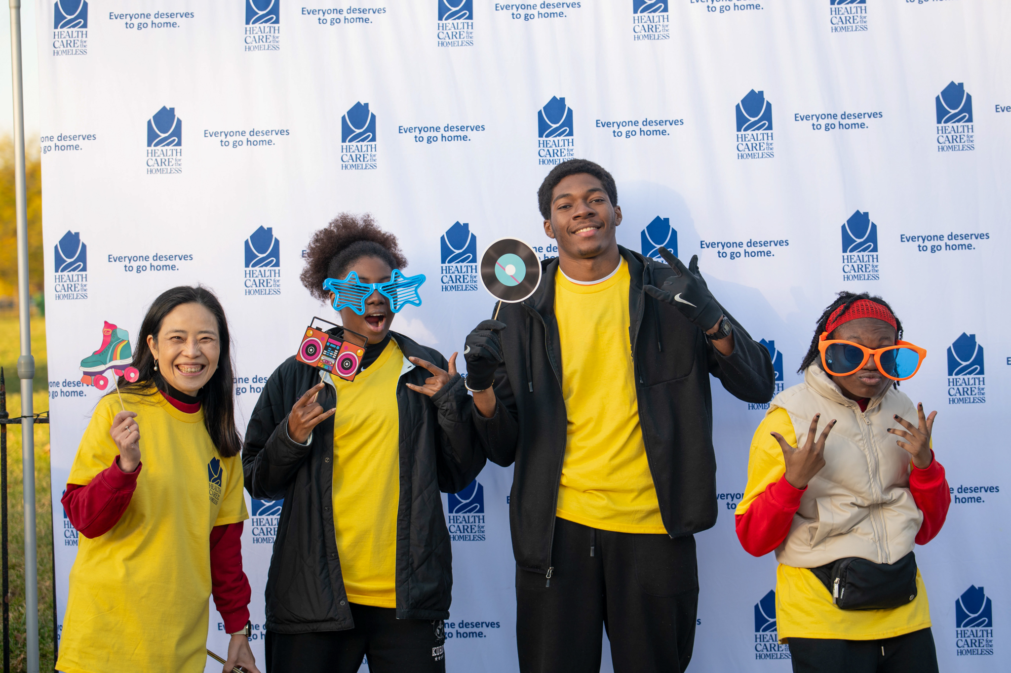 A group of four people wearing 80s props and yellow "volunteer" shirts pose in front of the step-and-repeat.