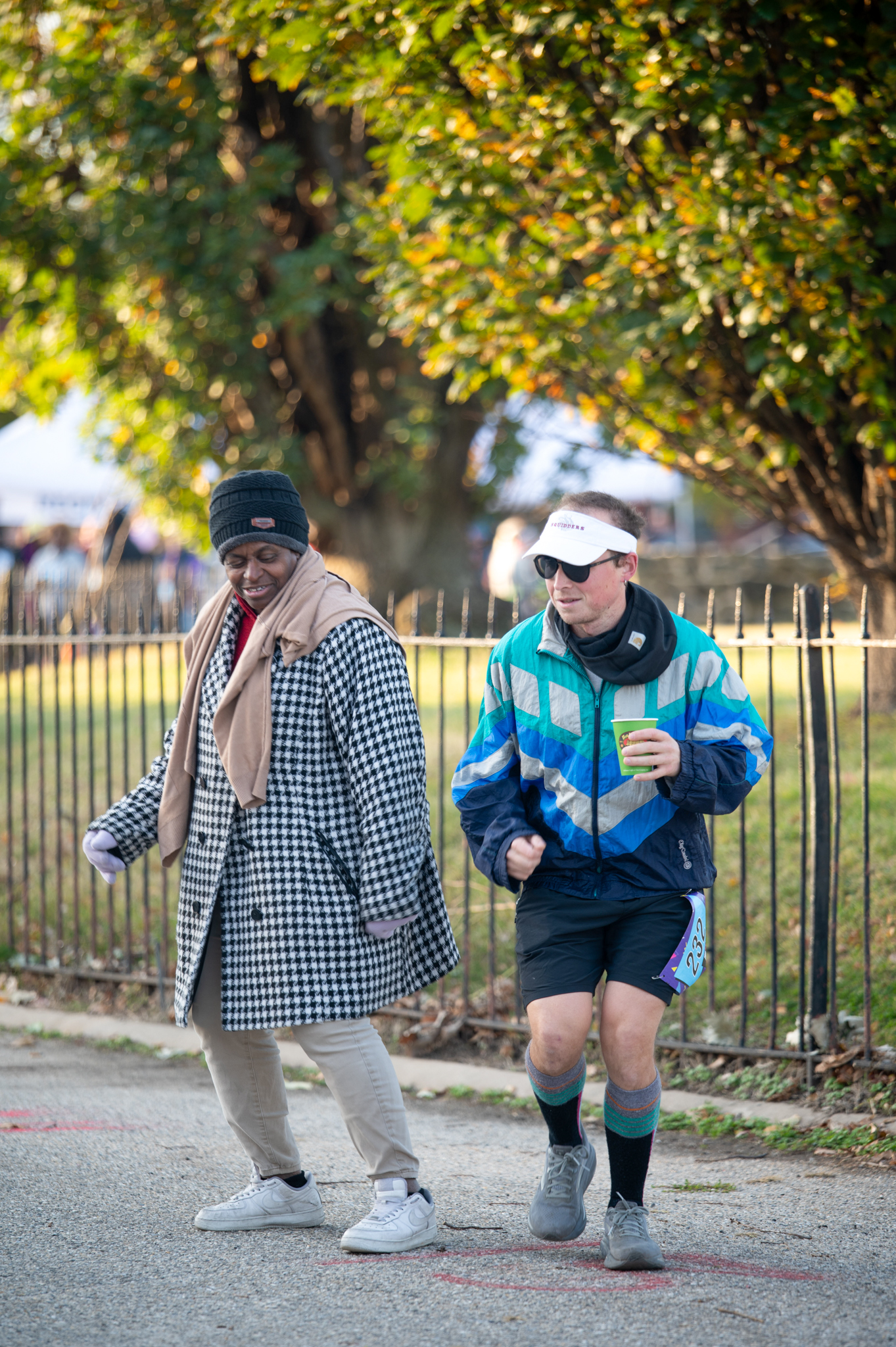 A dark-skinned woman in a black and white coat and a light-skinned man in a teal running suit dance.
