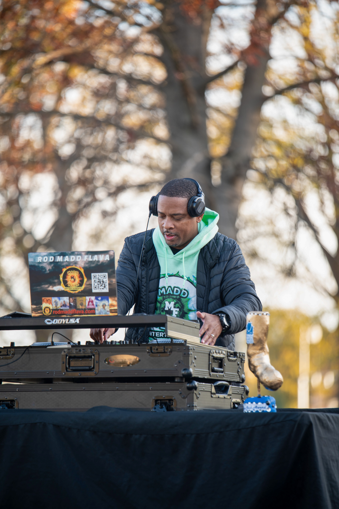 A dark-skinned man in a green hoodie and black jacket djs the music.