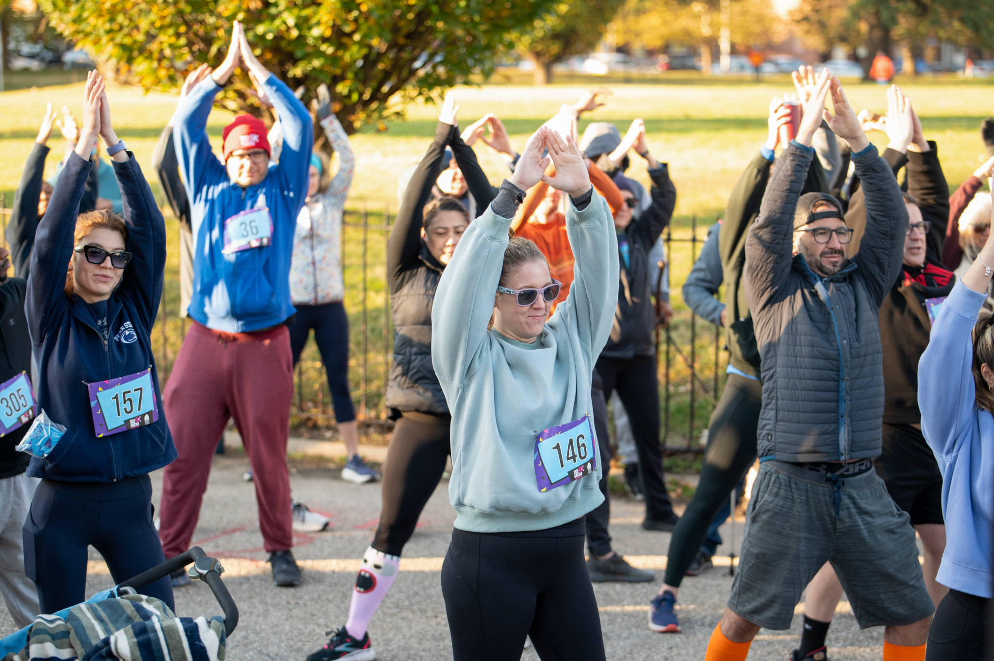 A group of 5K participants stretch with their hands over their head in a triangle.