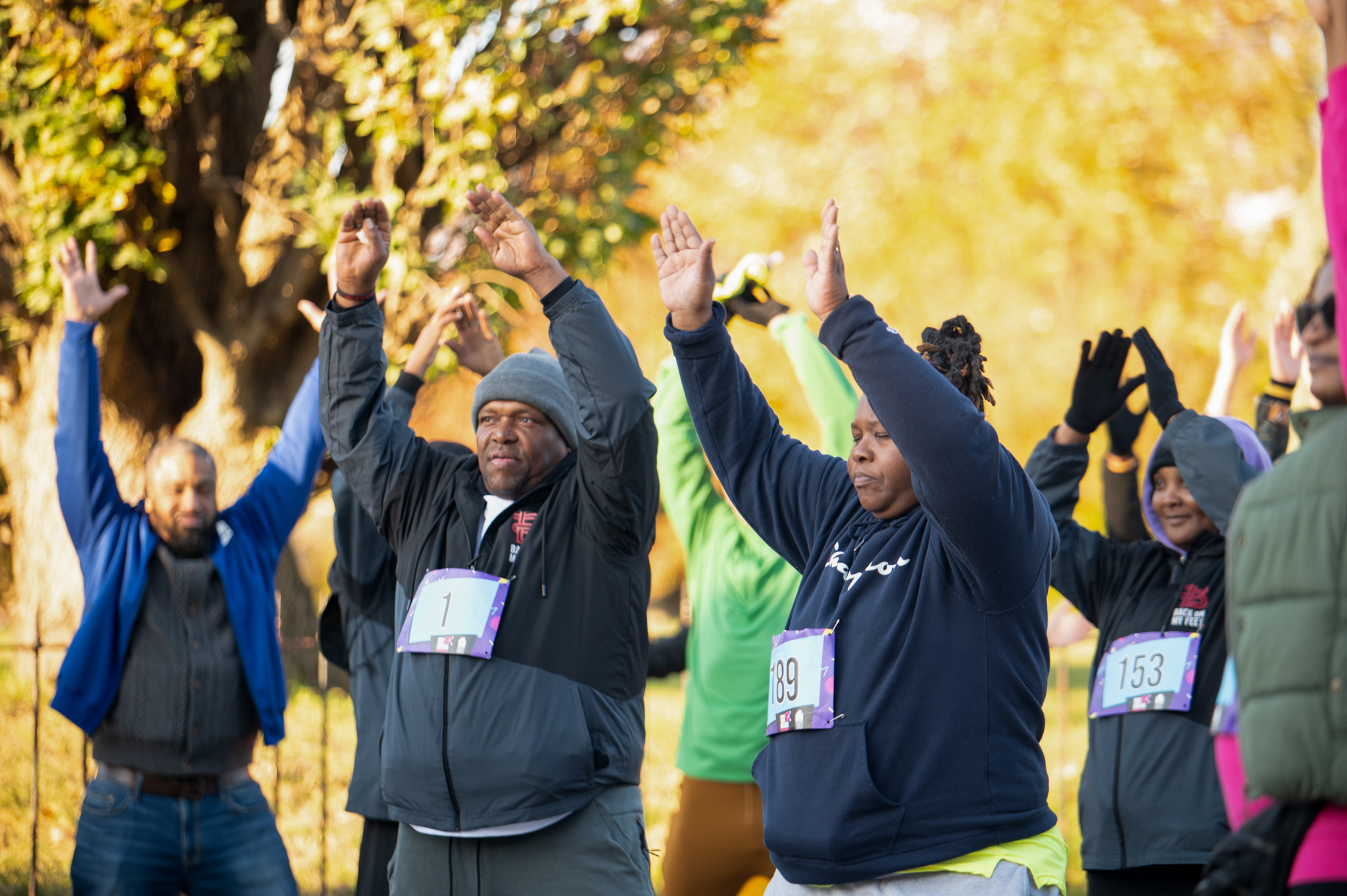 A group of 5K participants stretch with their arms above their heads.