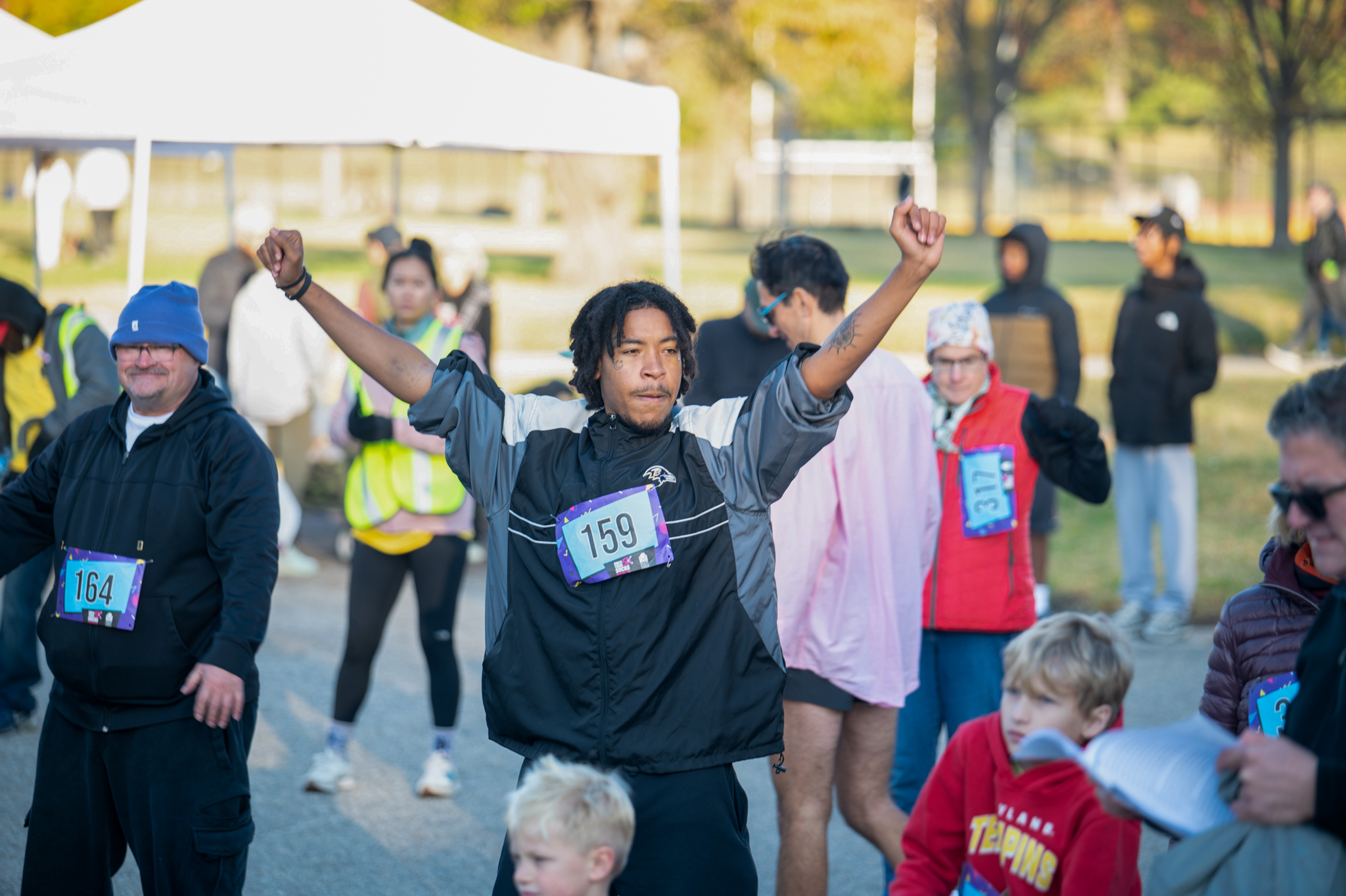 A young man with a grey jacket stretches his arms up.