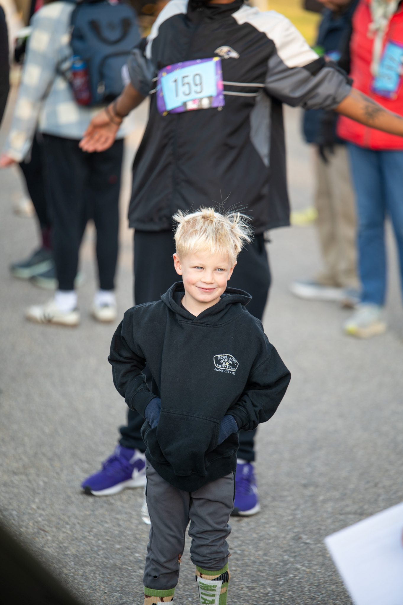 A light-skinned boy wearing a black hoodie and grey pants smiles.