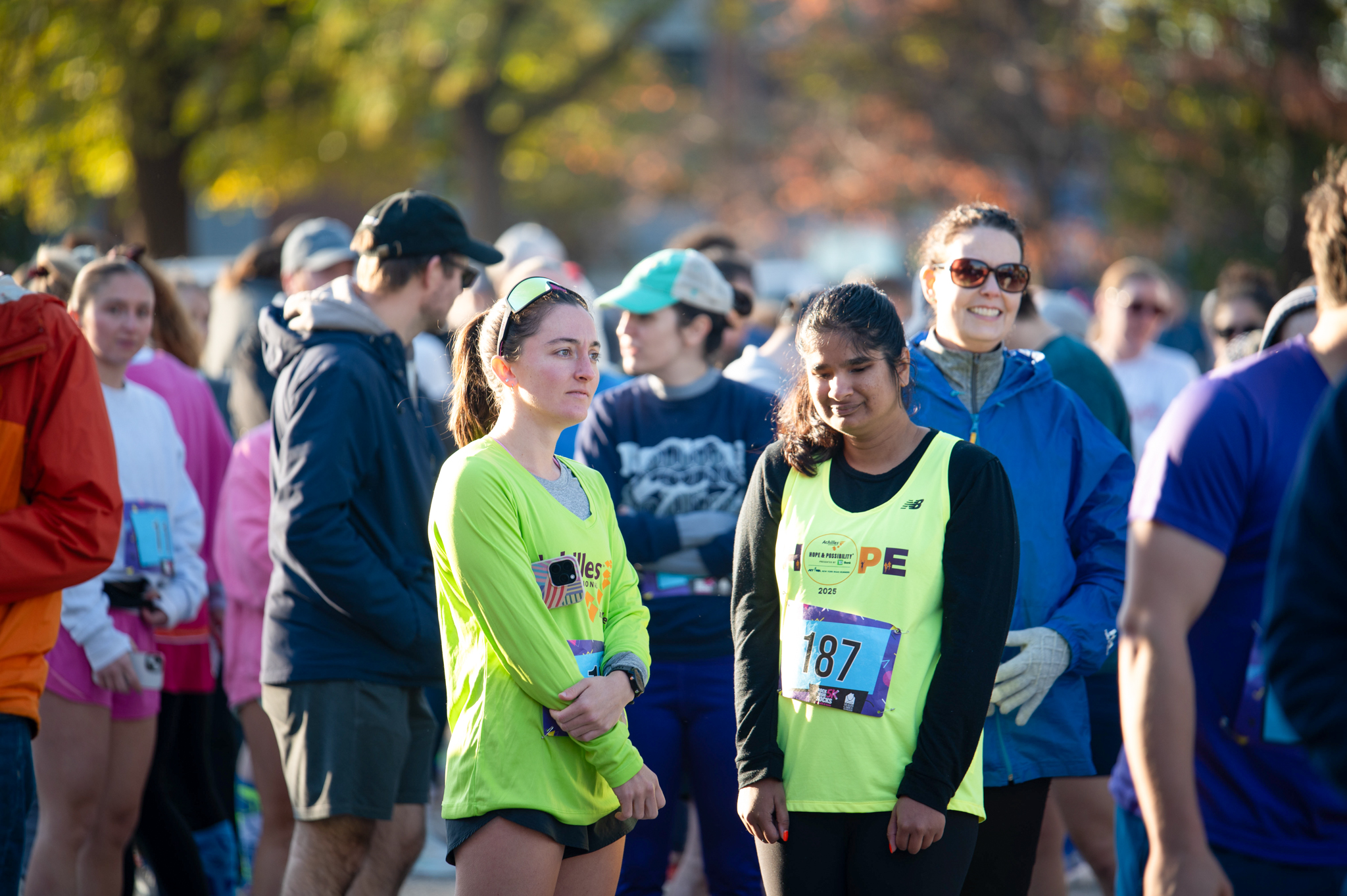 A light-skinned woman in a neon green top stands next to a medium-skinned woman in a neon top