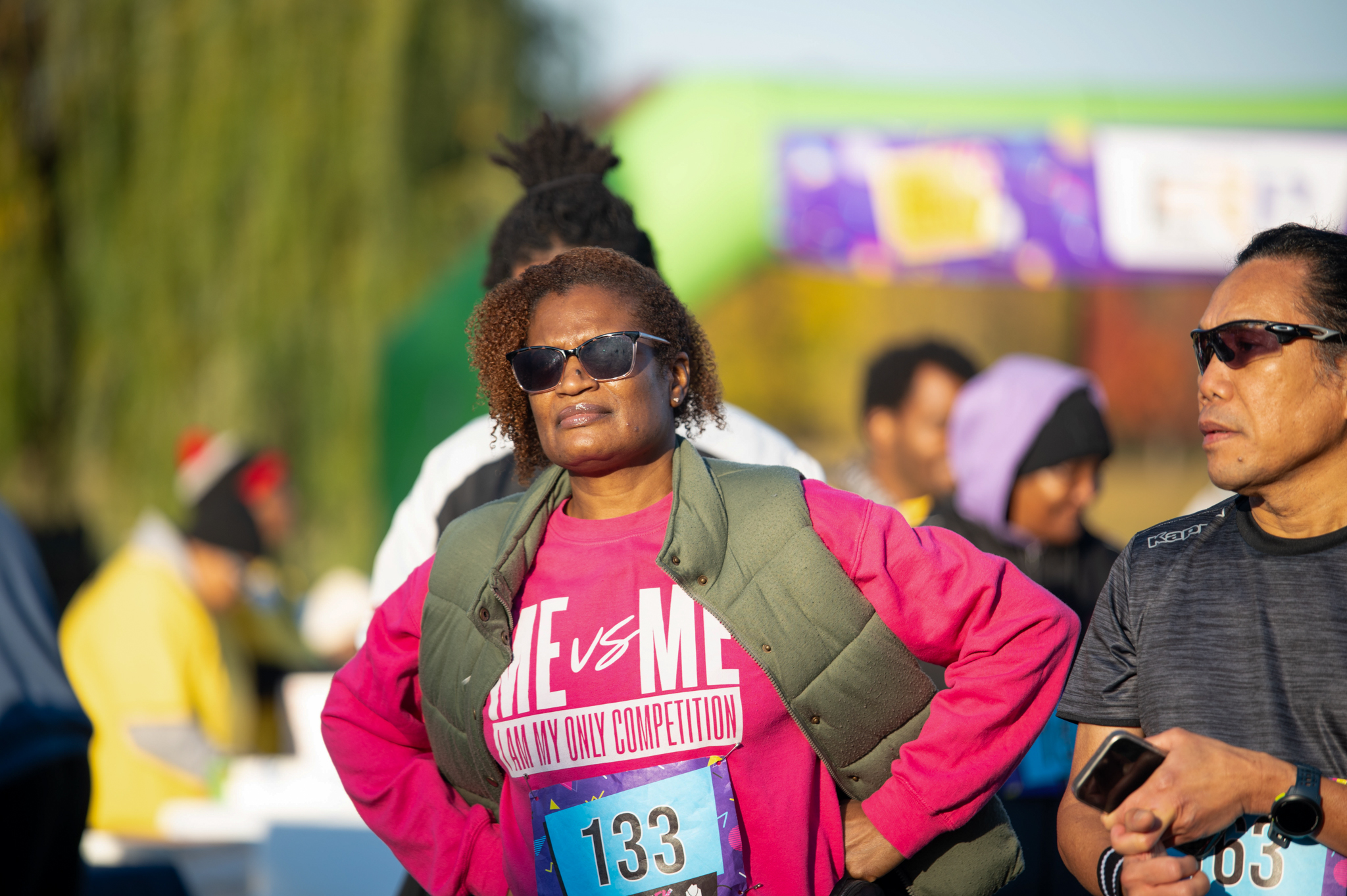 A medium-skinned woman in a pink long sleeve shirt with her hands on her hips.