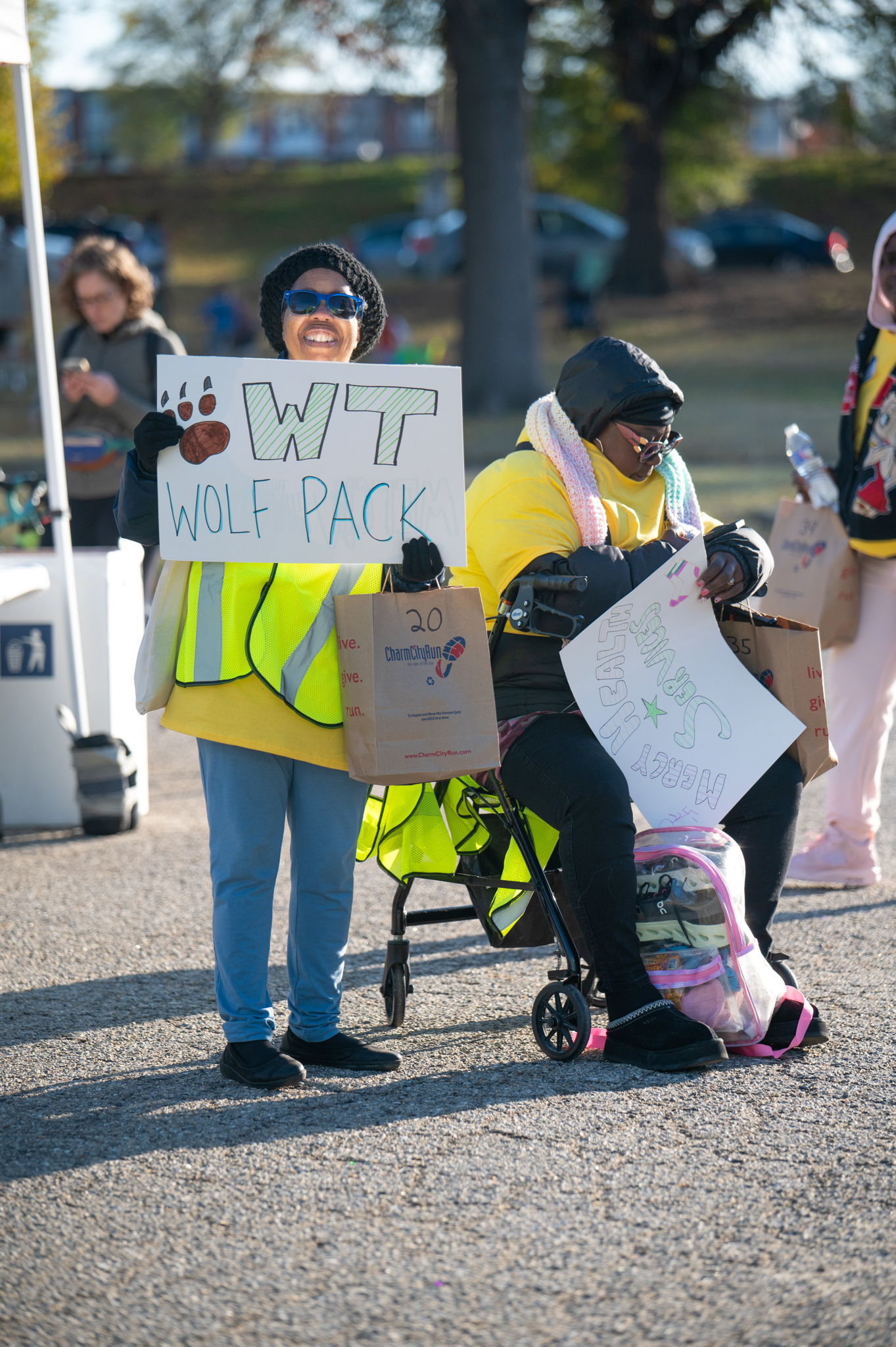 Two women wearing yellow "volunteer" shirt hold signs to cheer on 5K teams