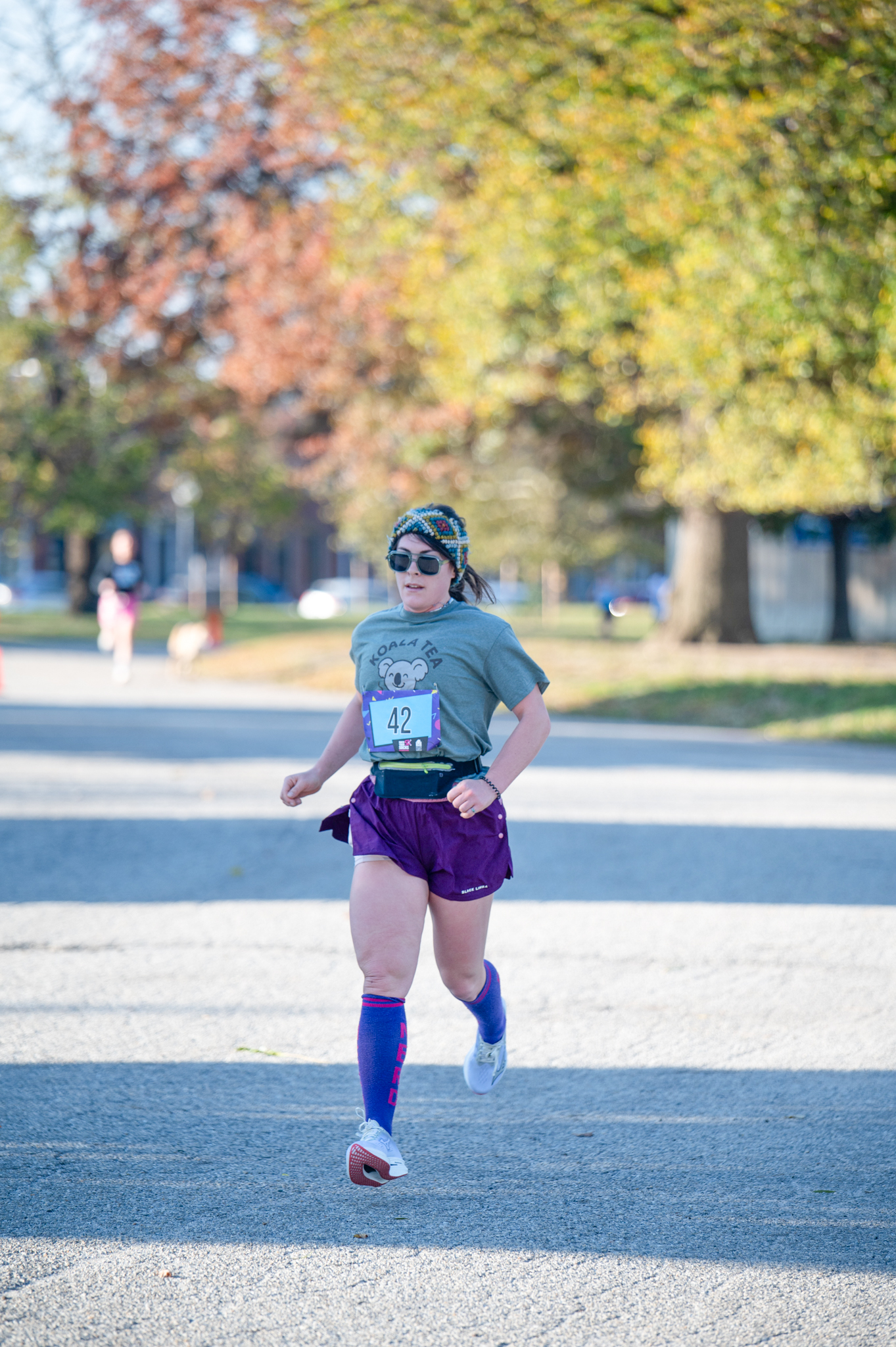 A light-skinned woman runs in a teal shirt and purple shirts