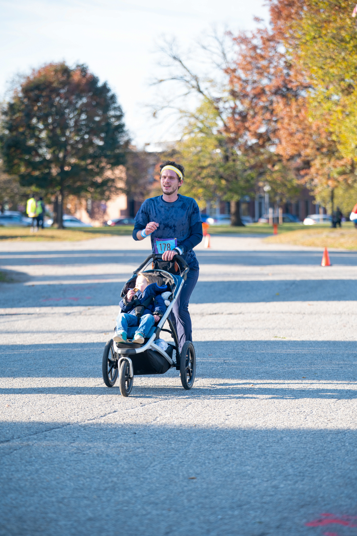 A light-skinned man runs in a blue shirt, pushing a stroller with a child