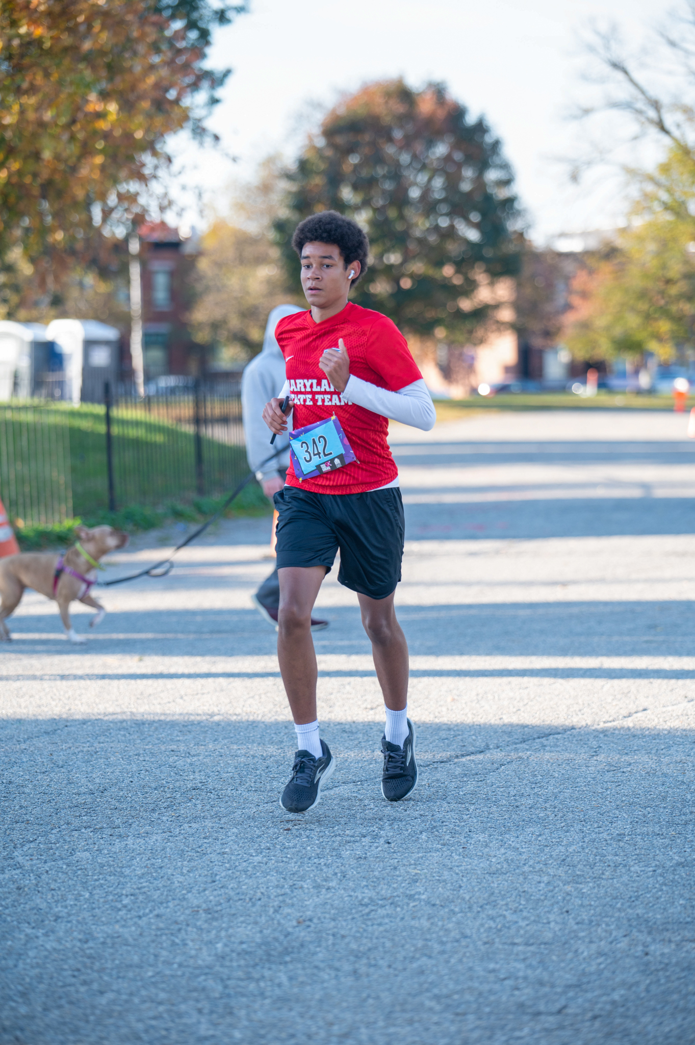 A medium-skinned young man runs with a red shirt and black shorts