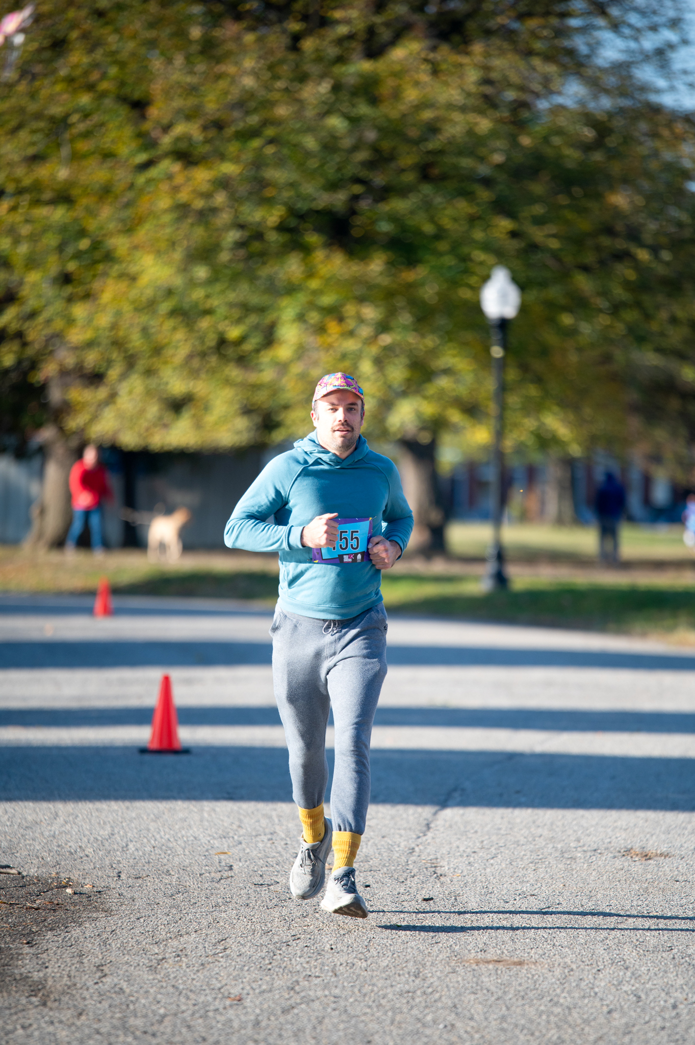 A light-skinned man in a blue long sleeve shirt and grey pants runs