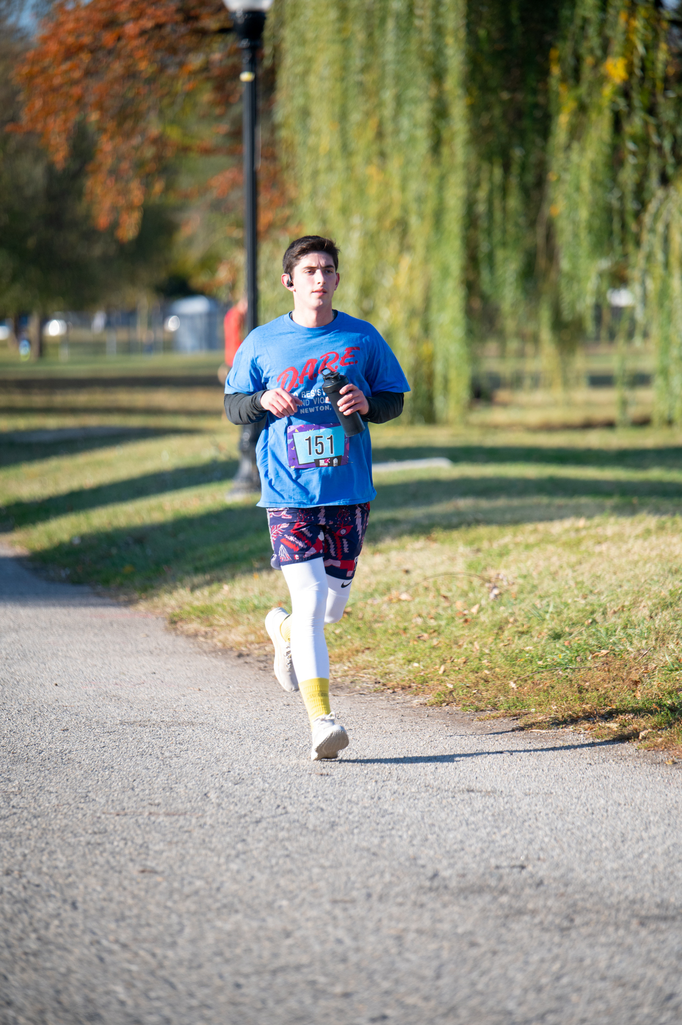 A light-skinned man in a blue long sleeve shirt and purple shorts runs