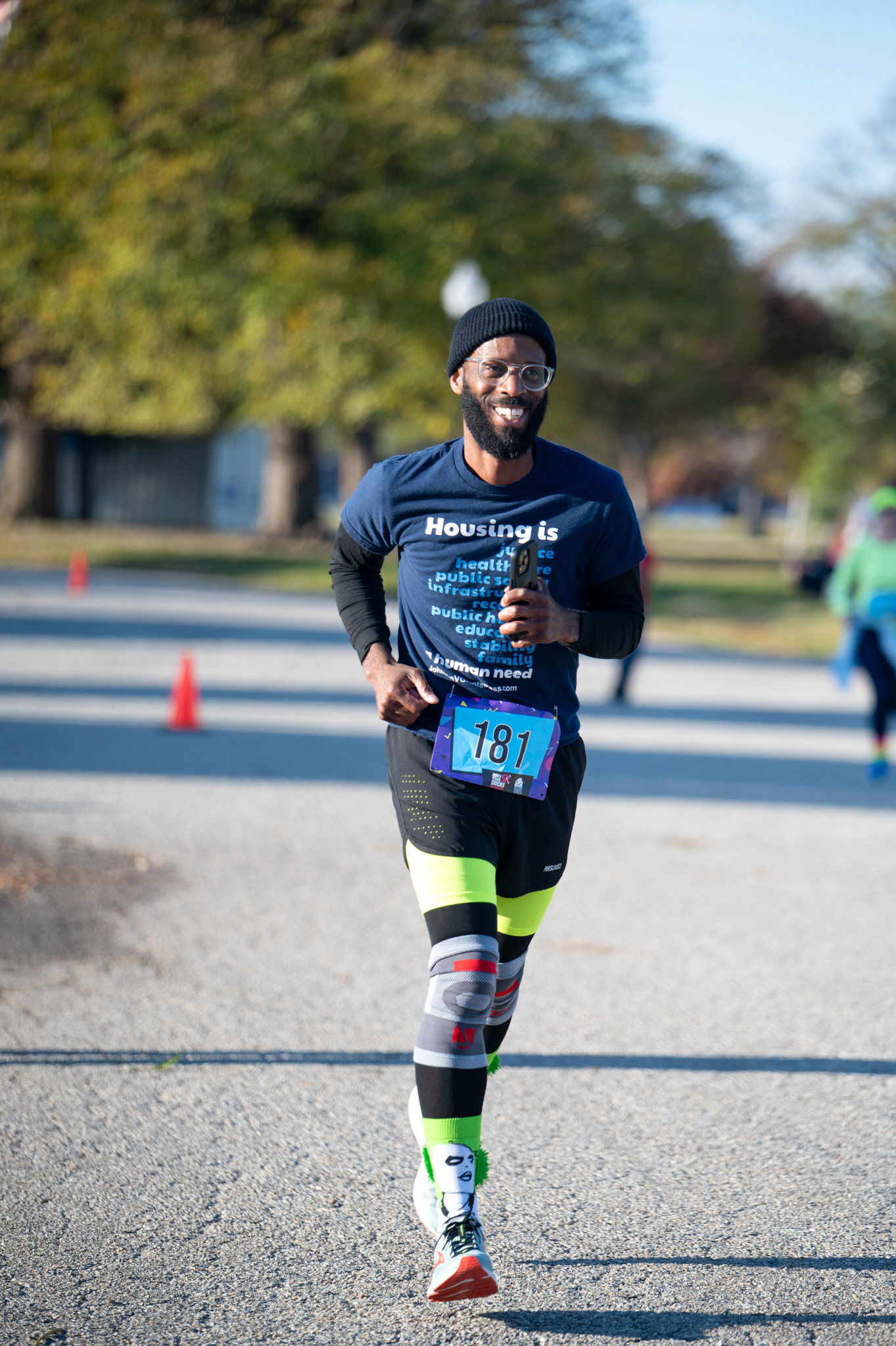 A dark-skinned man in a blue shirt sleeve shirt over a black long sleeve shirt jogs