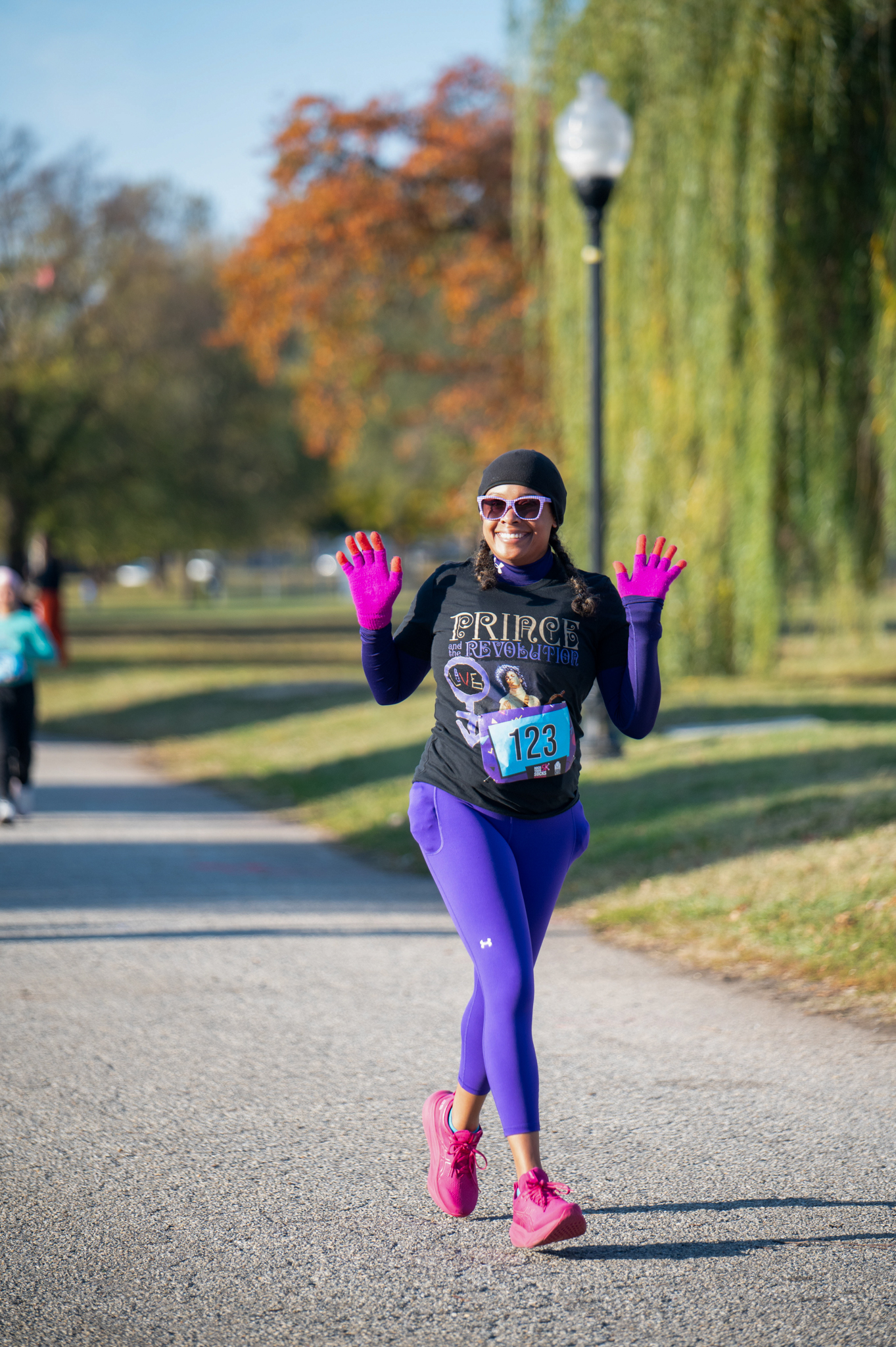 A medium-skinned woman jobs in a black shirt with purple leggings and pink gloves.