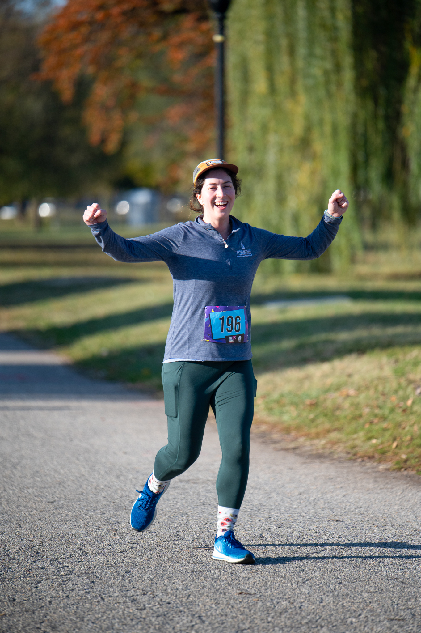 A light-skinned woman in a blue athletic top and green leggings jogs