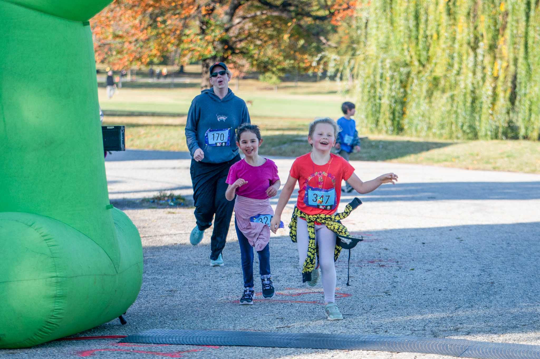 Two light-skinned girls cross the finish line under the green inflatable arch