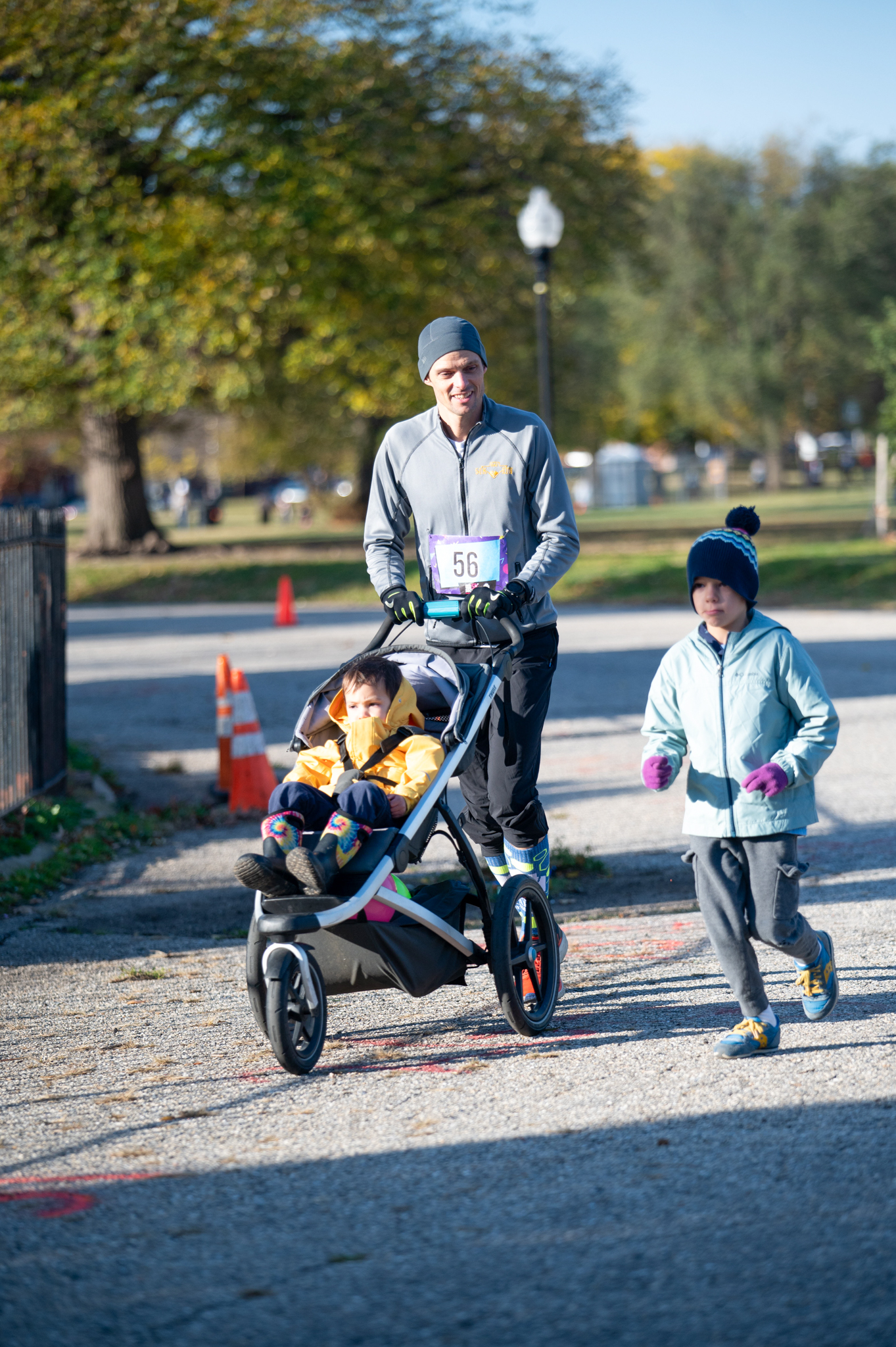 A light-skinned man jogs alongside a child while pushing a stroller