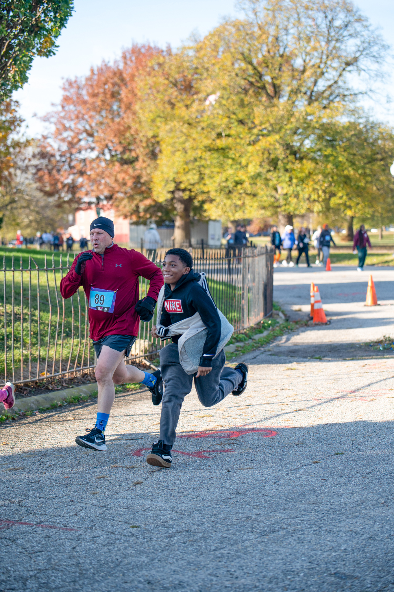 A light-skinned man in a red athletic top and a dark-skinned boy in a black hoodie sprint to the finish line