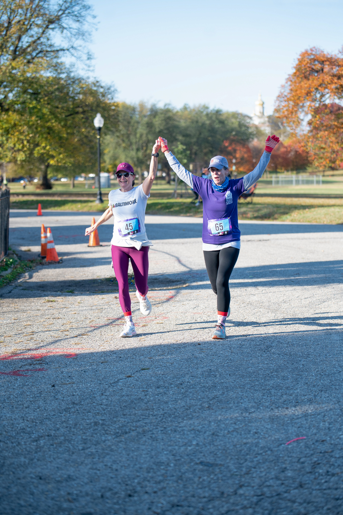 A light-skinned woman in a white top and purple leggings holds the hand of a light-skinned woman in a purple top and black leggings