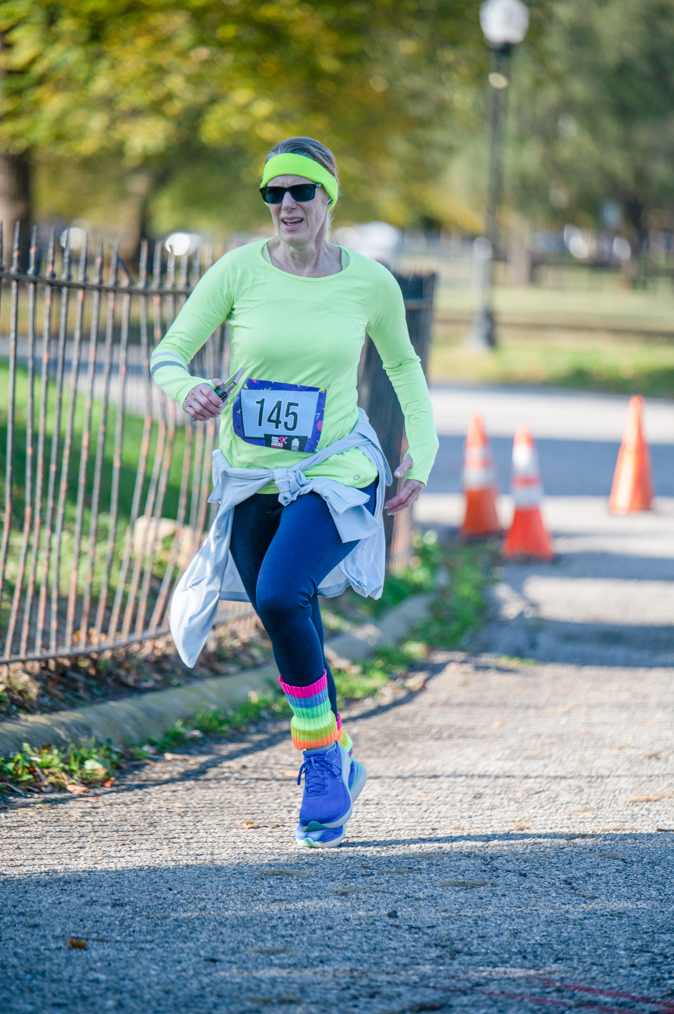 A light-skinned woman in a neon green top and blue leggings jogs