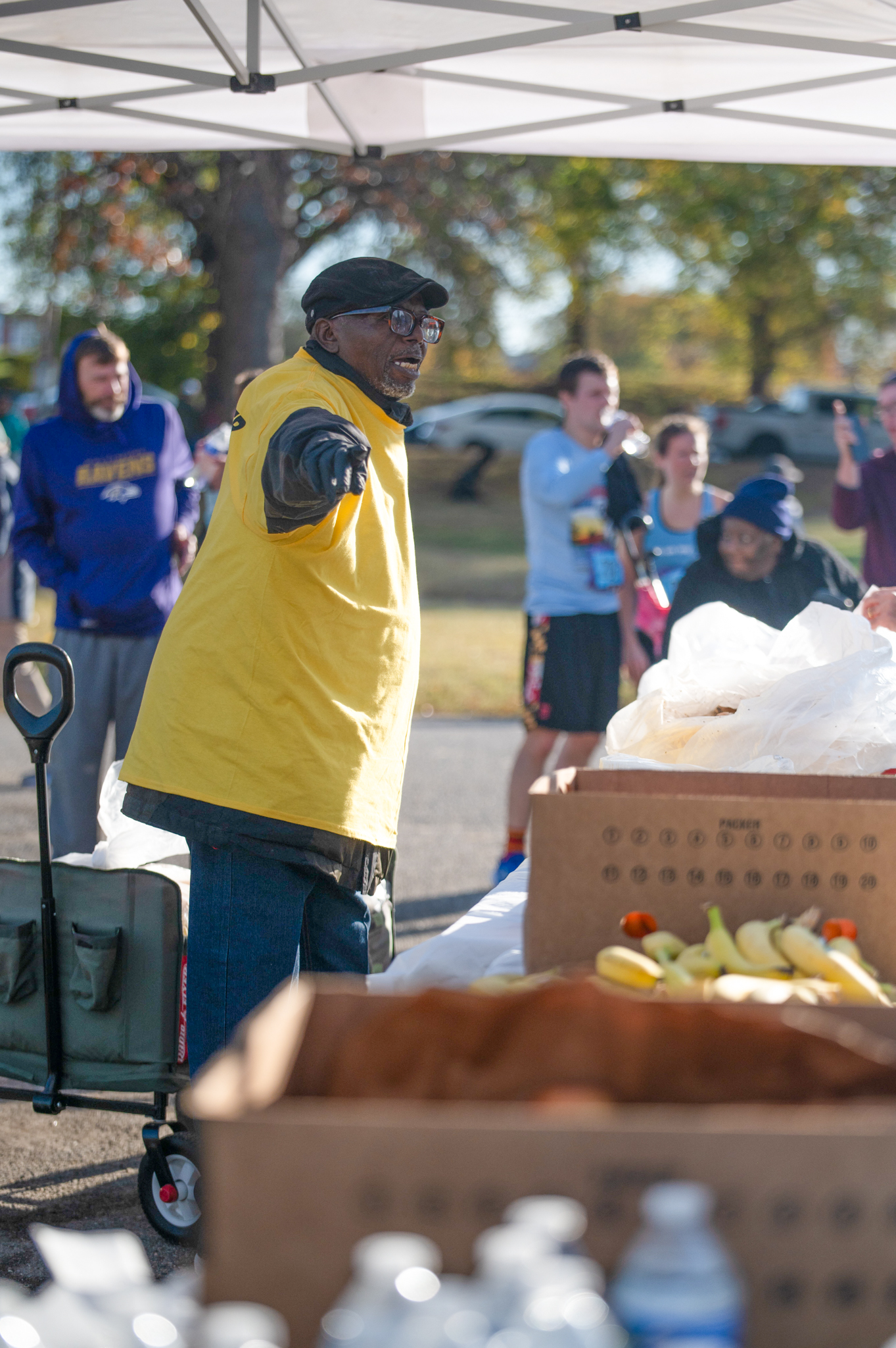 A dark-skinned man in a yellow volunteer shirt points while standing at a table with snacks