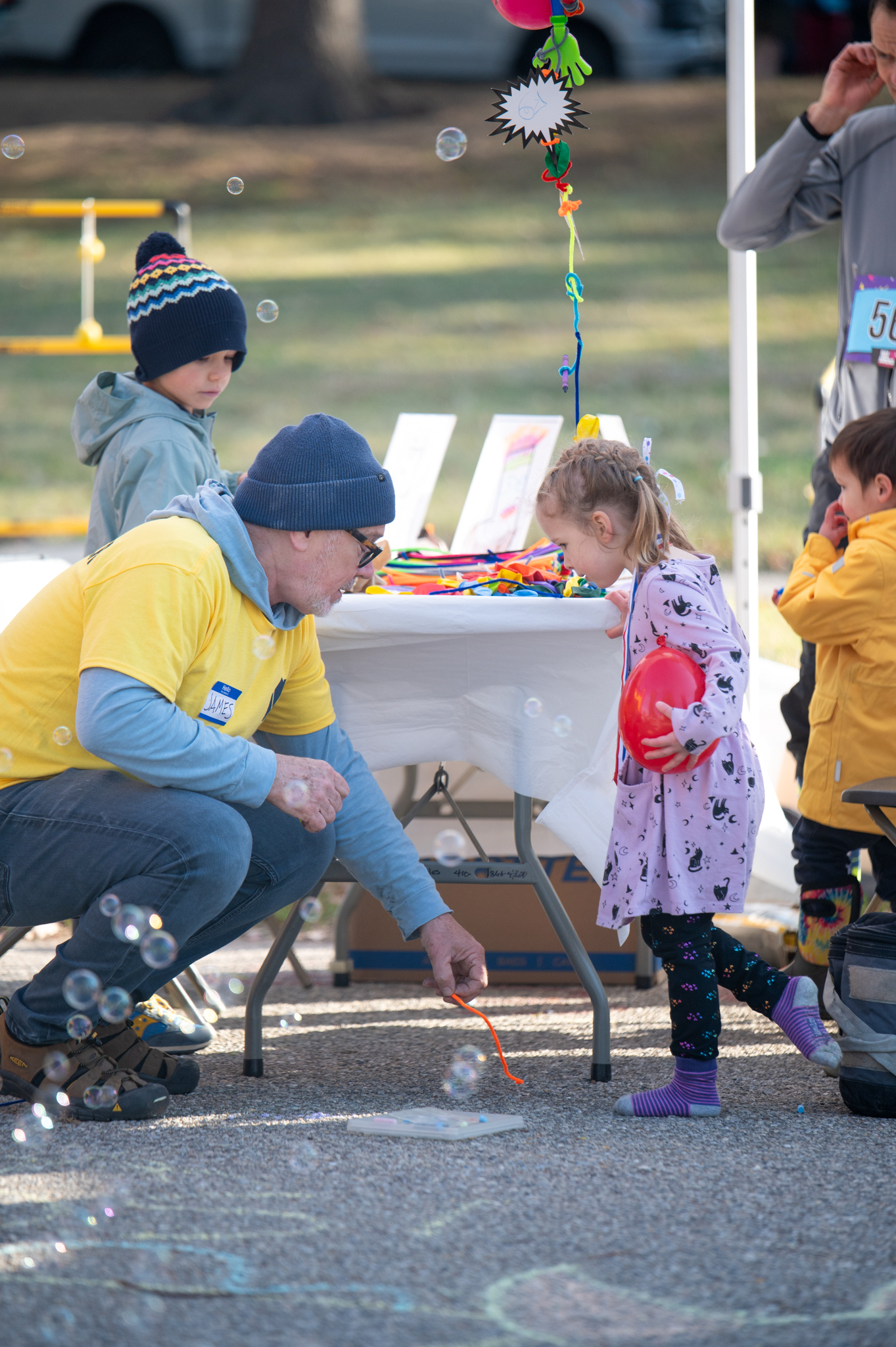 A light-skinned man wearing a yellow shirt kneels next to a light-skinned girl in a dress