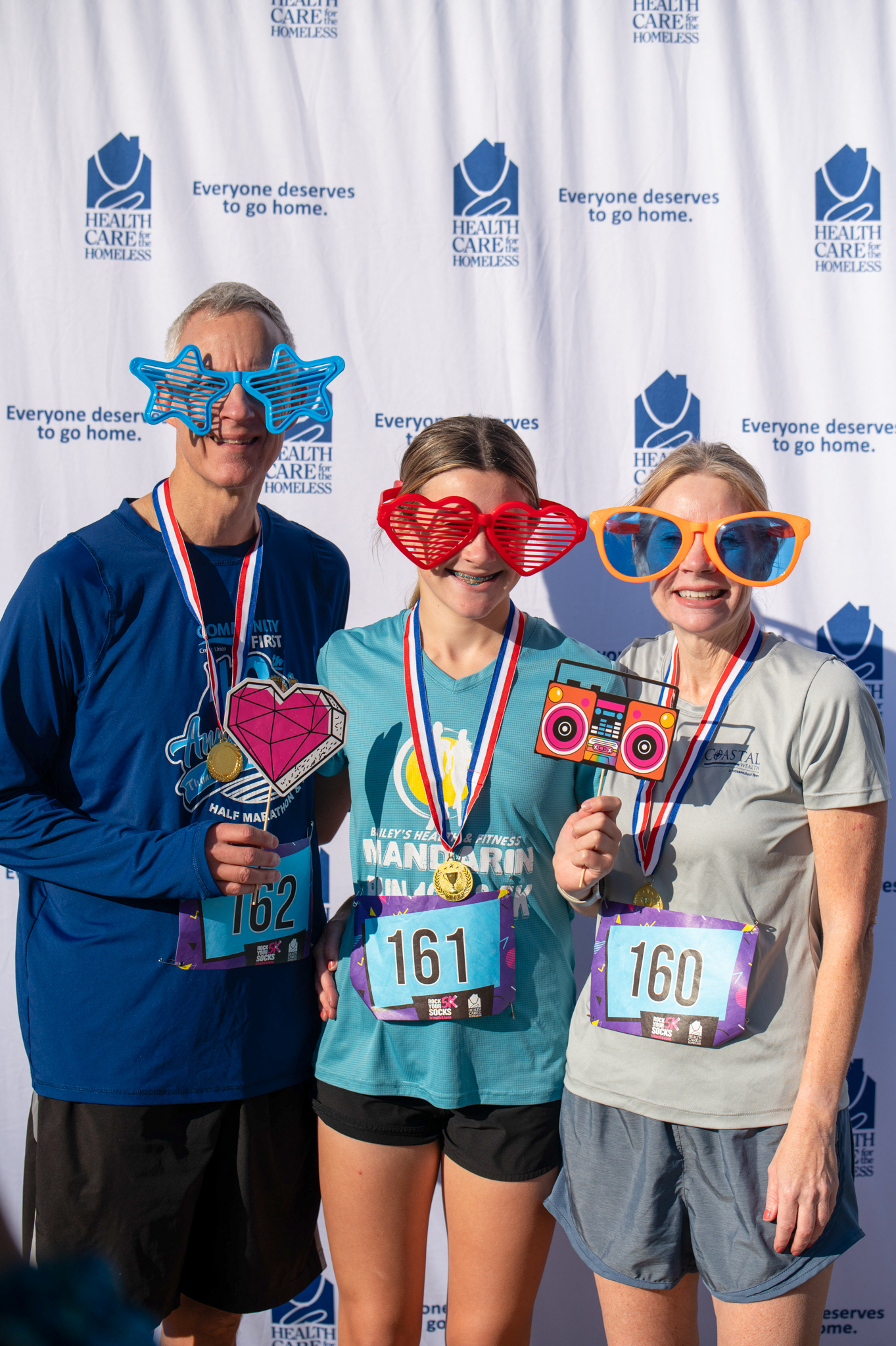 Three light-skinned people wear 80s props and smile in front of the step-and-repeat