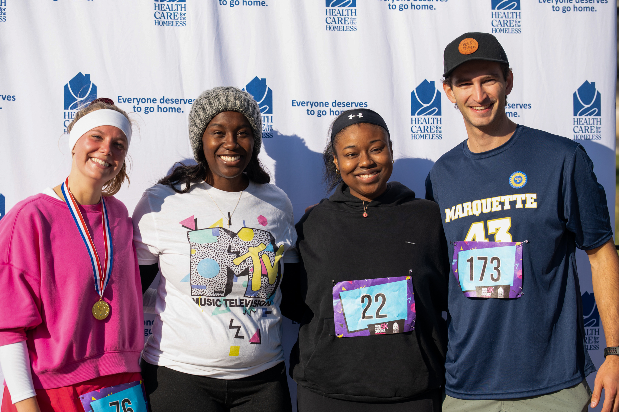 Four people smile in front of the Health Care for the Homeless step-and-repeat