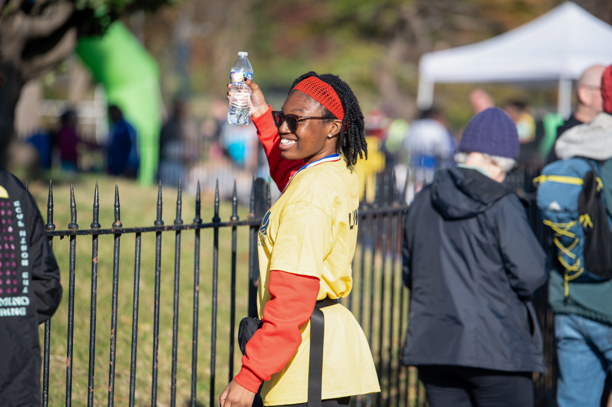 A dark-skinned woman wearing a yellow volunteer shirt holds a water bottle