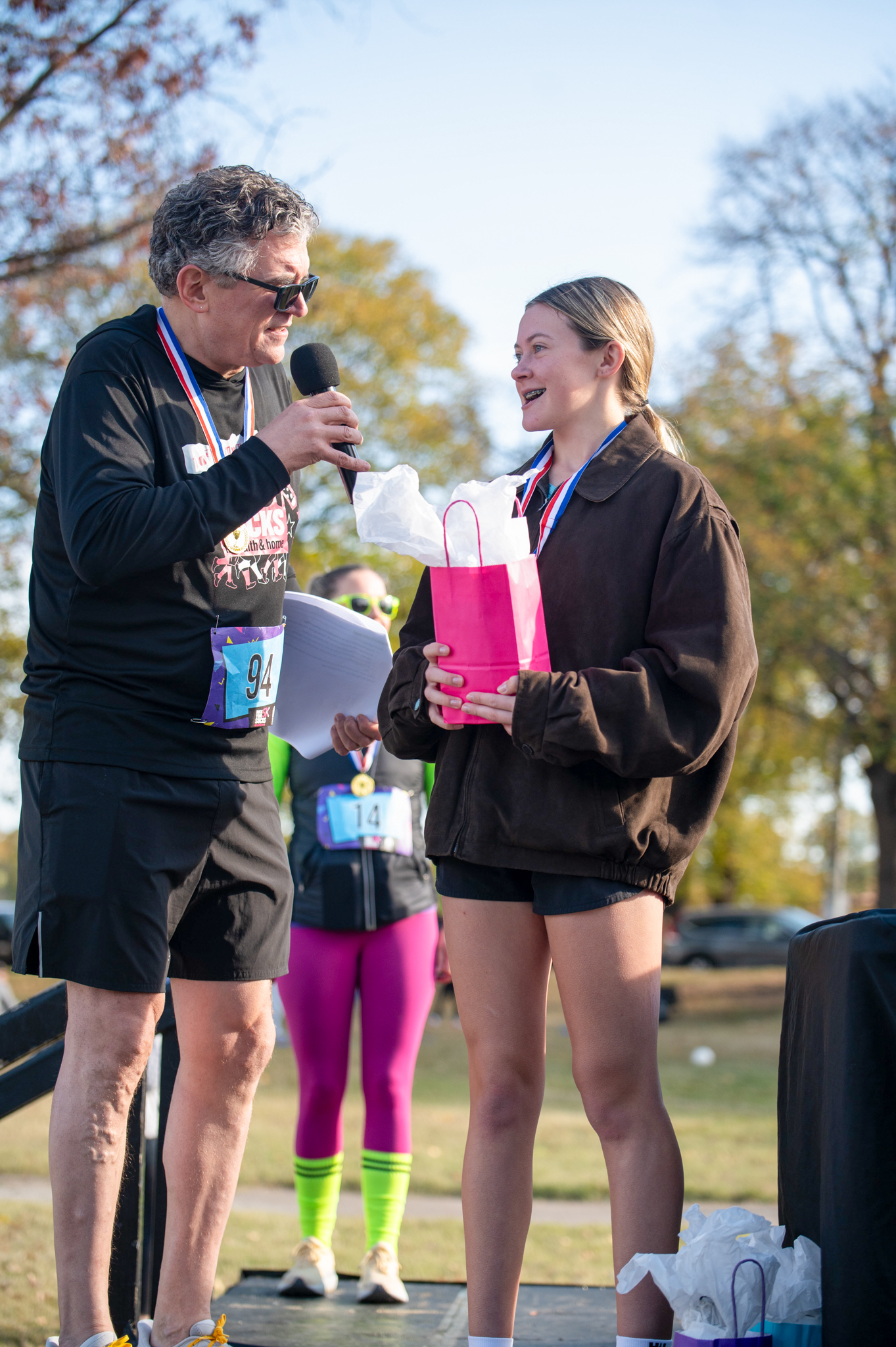 A light-skinned man holding a microphone speaks to a light-skinned girl holding a pink gift bag