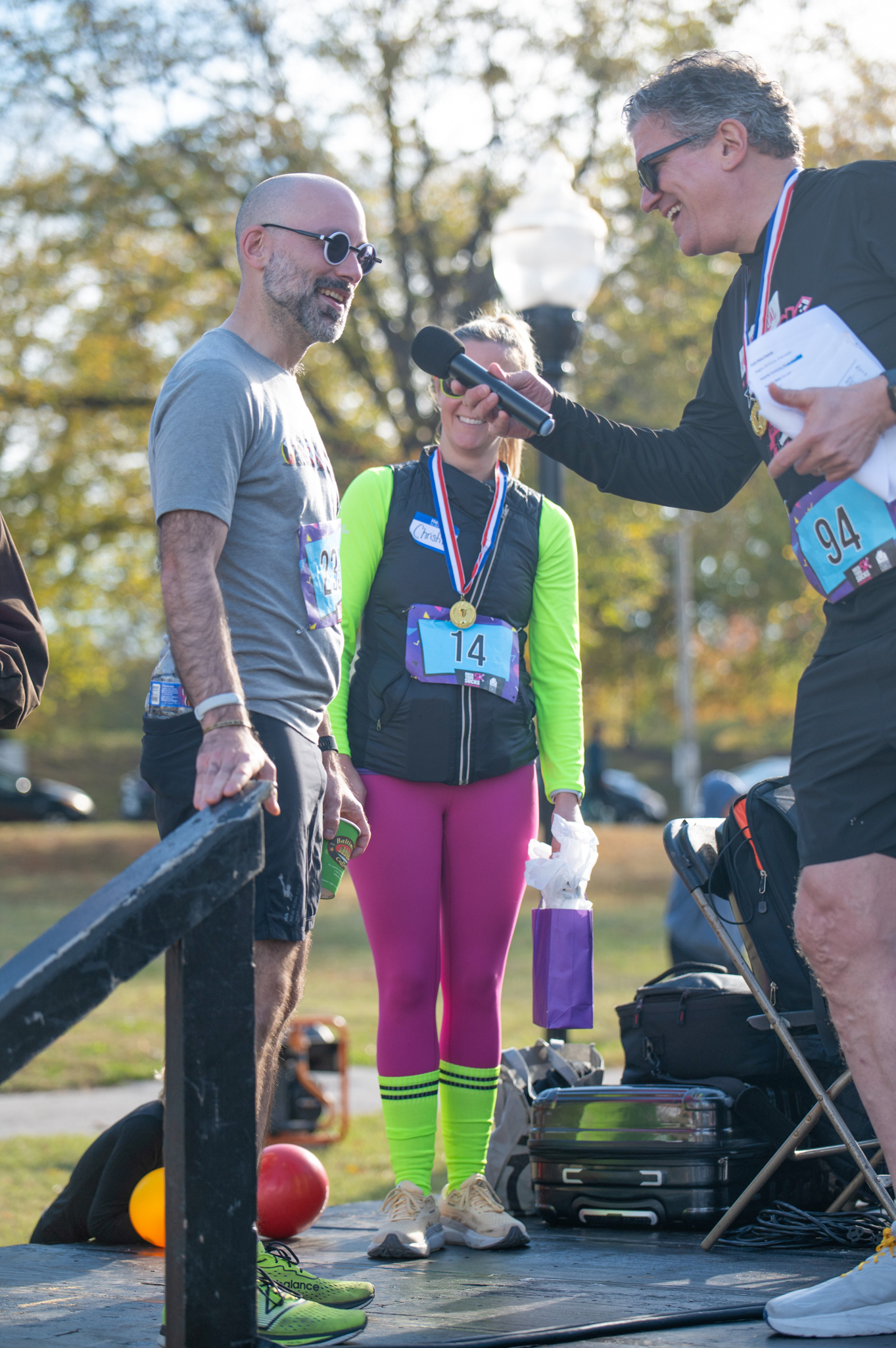 A light-skinned man holding a microphone speaks to a light-skinned man wearing a grey shirt.