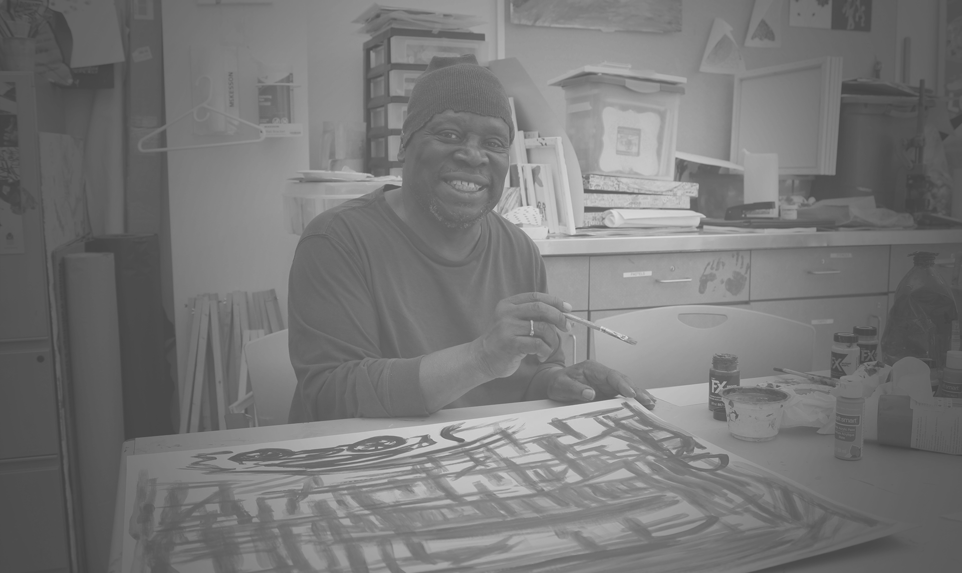 Black and white image of a smiling dark-skinned man wearing a hat while painting