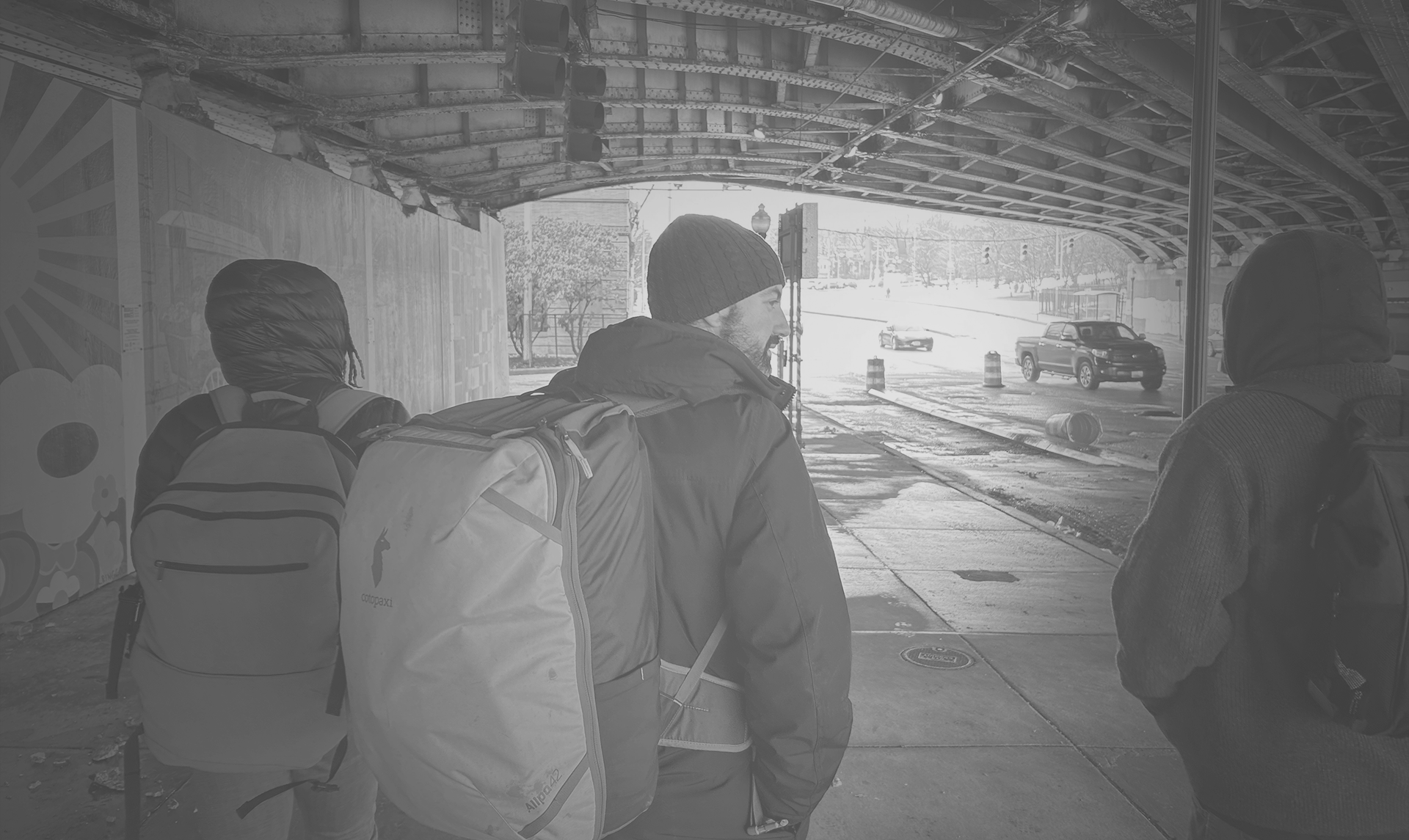 Three members of the street medicine team walk under an overpass, wearing backpacks and winter coats.