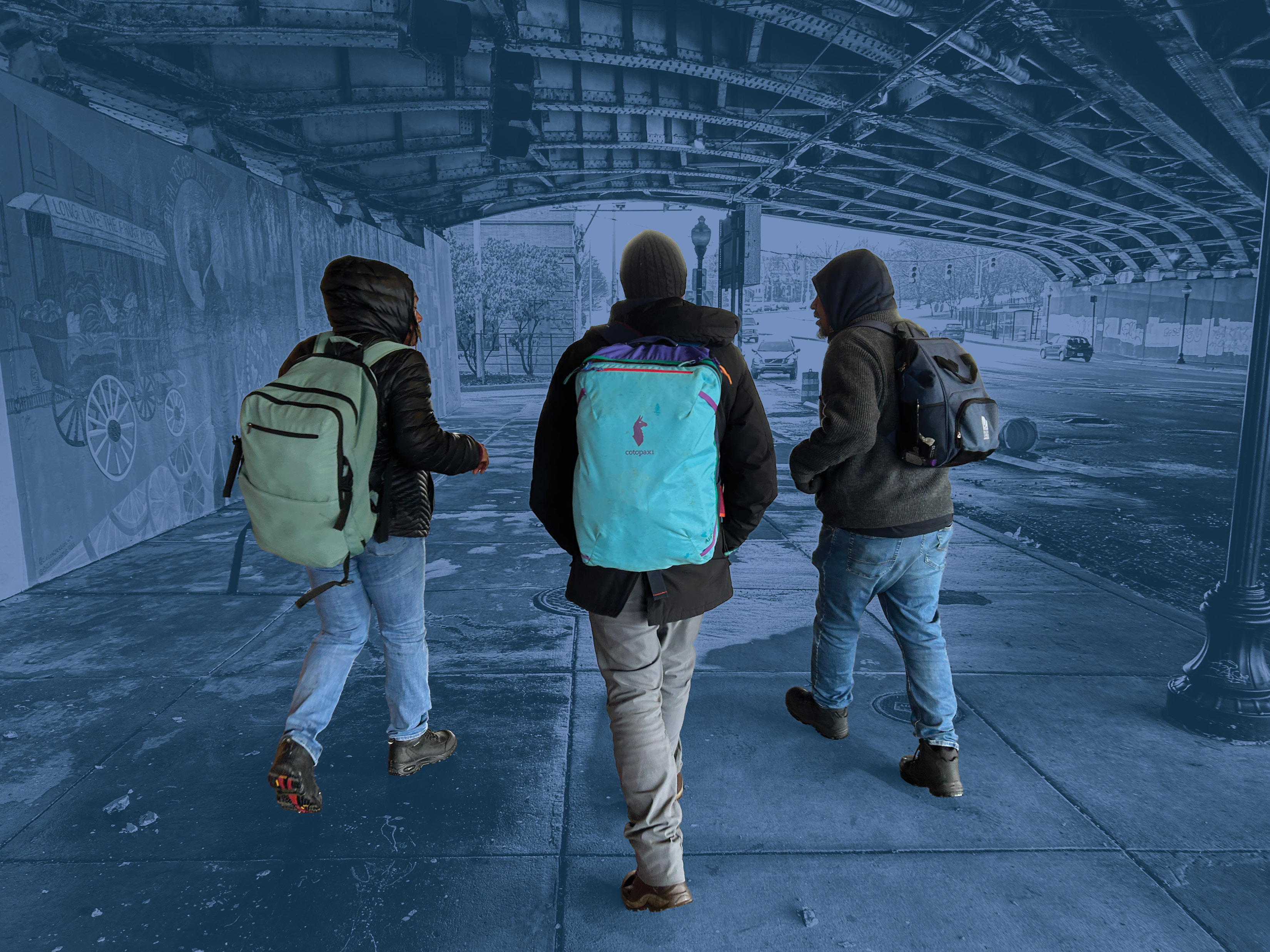 The backs of three people in pants, jackets and with big backpacks on. They are walking under a bridge side-by-side. The people are in full color. Their surroundings have a blue filter. 