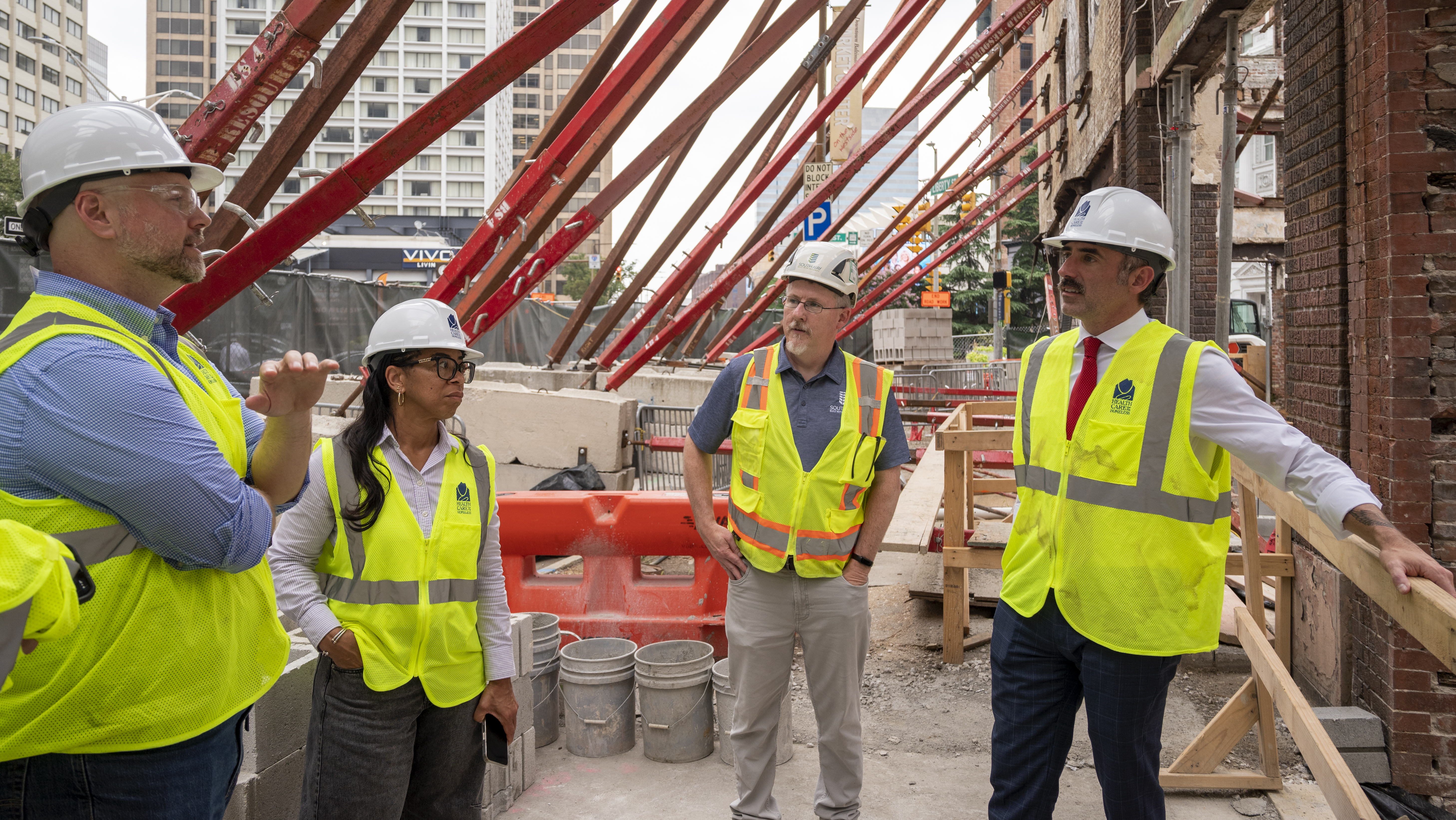 Four people in reflective vests and hardhats stand near orange scaffolding.