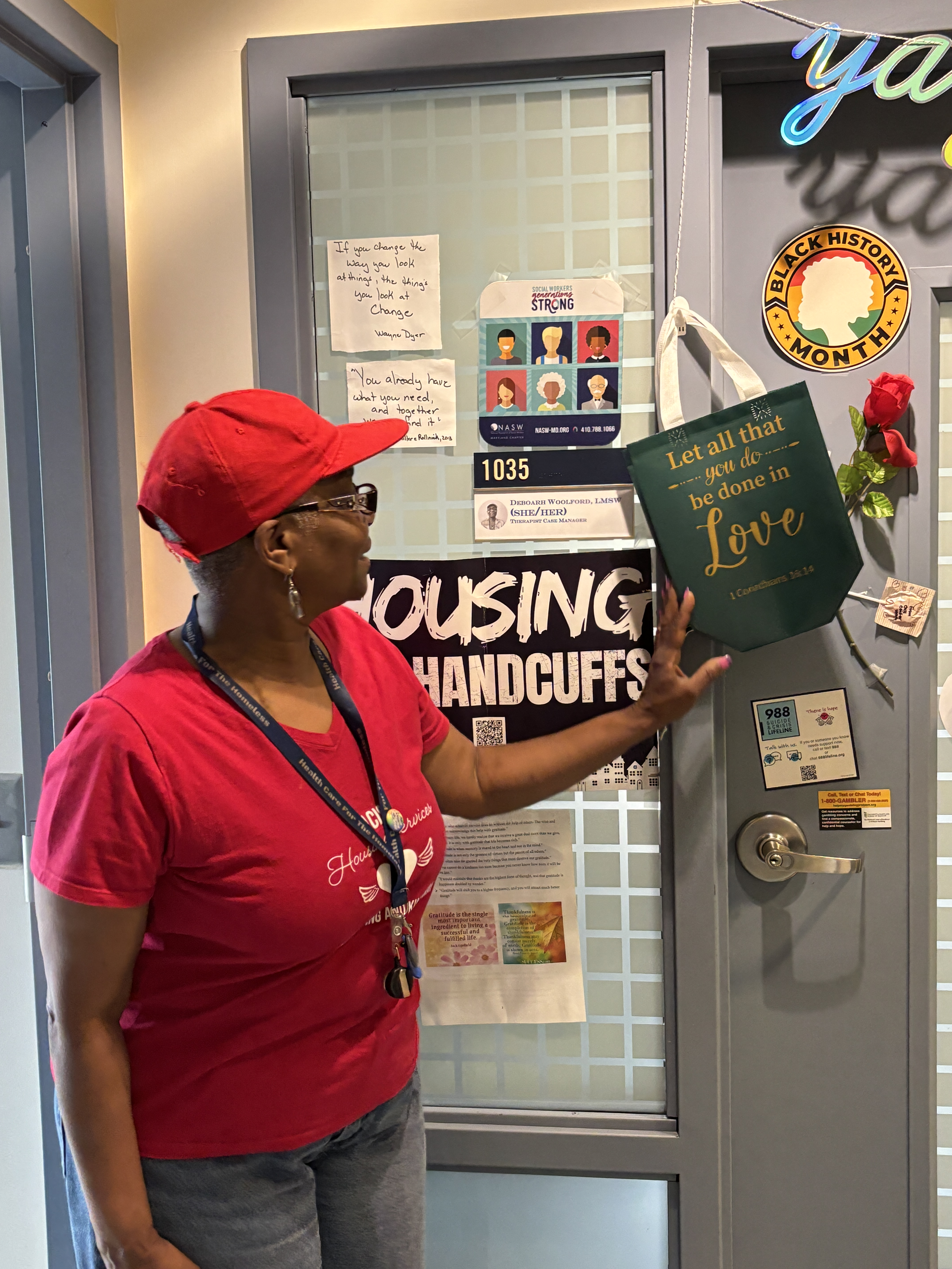 A woman points to a green tote bag tacked to an office door.