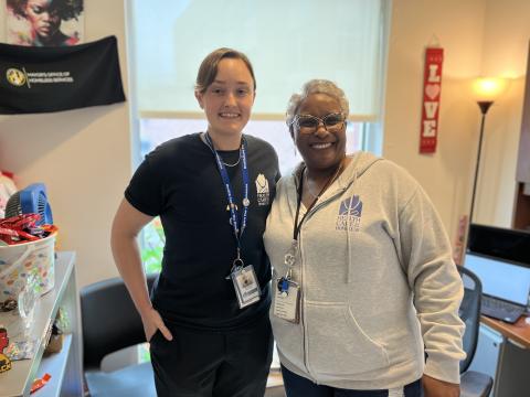 Alex James, RN, LMSW (L), a light-skinned person with short brown hair, stands next to Tammy Montague, PhD, LCSW-C (R), a dark-skinned woman with glasses and short grey hair.