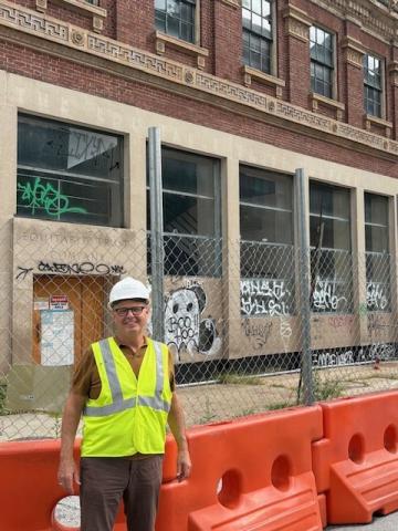 A light-skinned man in a hard hat and vest standings in front of the future site of Sojourner Place at Park.