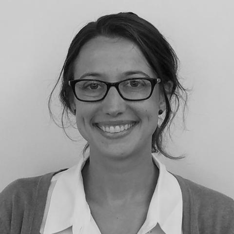 A black and white headshot of a light-skinned woman with glasses and hair pulled back.