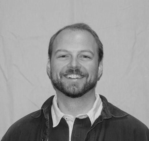 A black and white headshot of a light-skinned man with short hair and facial hair.